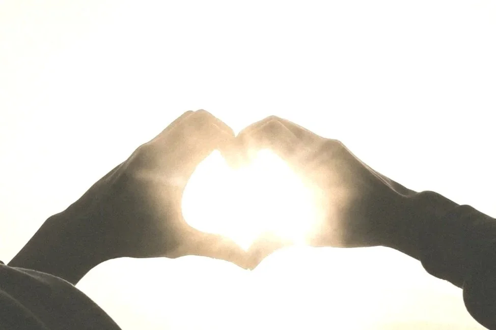 Hands forming a heart shape with the sun shining through the center