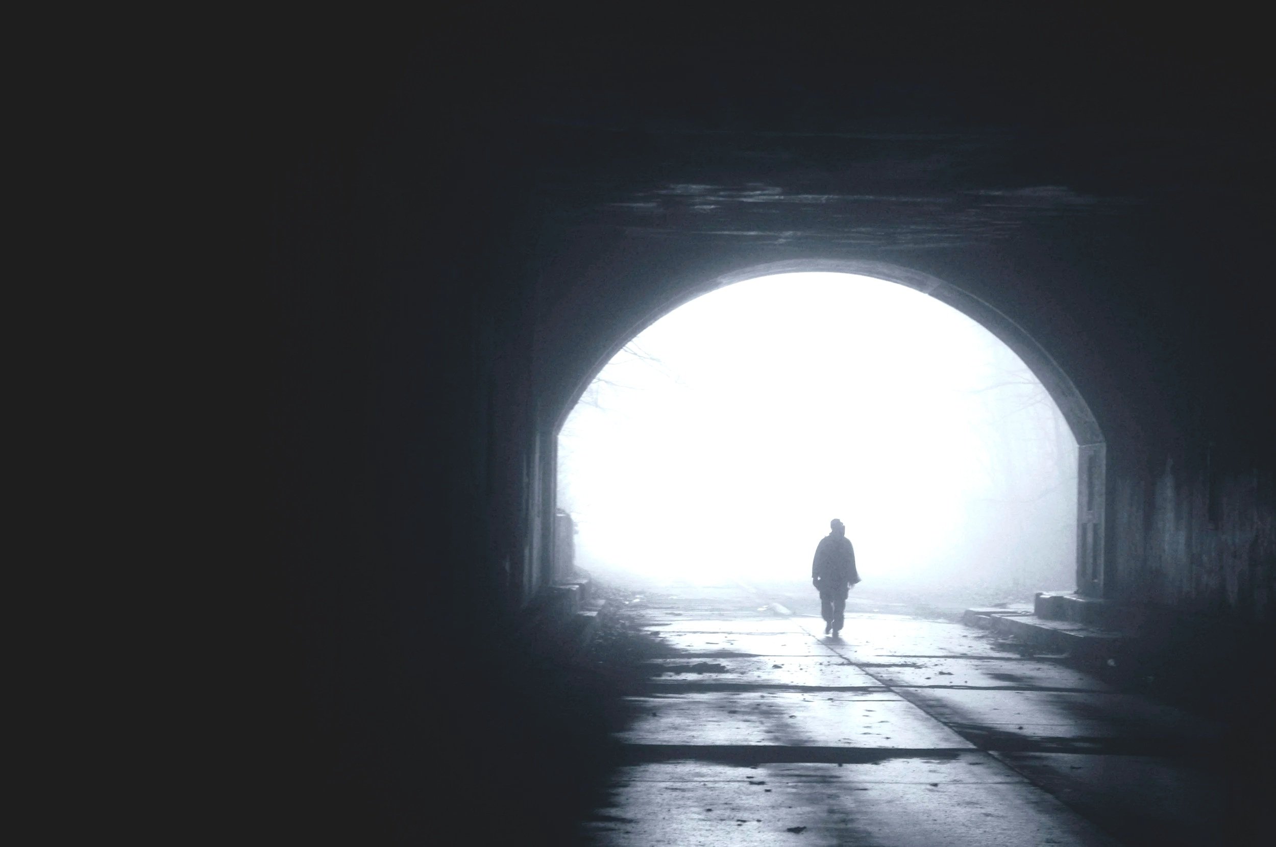 Silhouetted figure walking in a lonely tunnel toward light, representing feelings of isolation and emotional pain for the weary survivor of trauma and complex PTSD approaching a healing journey of finding hope, resilience, and renewed purpose.