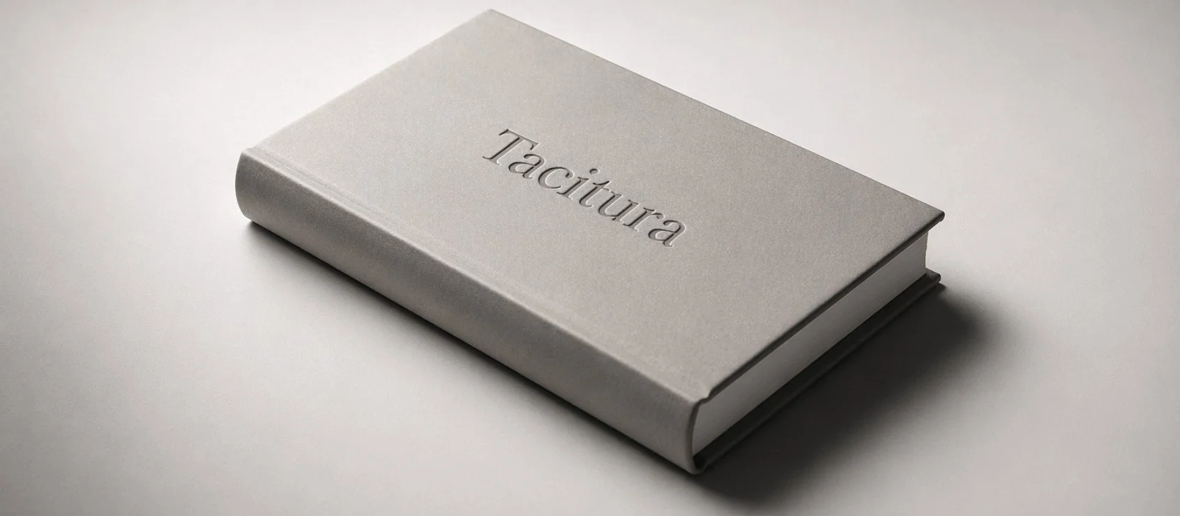 A closed, silver hardcover book with the word 'Tacitura' embossed on the cover, resting on a plain light gray surface.
