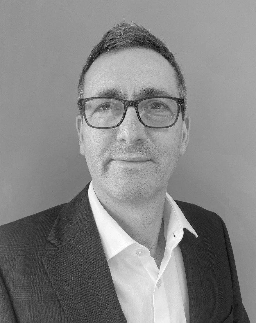 Black and white portrait of David Panni in a suit, wearing glasses, smiling faintly, against a plain background.