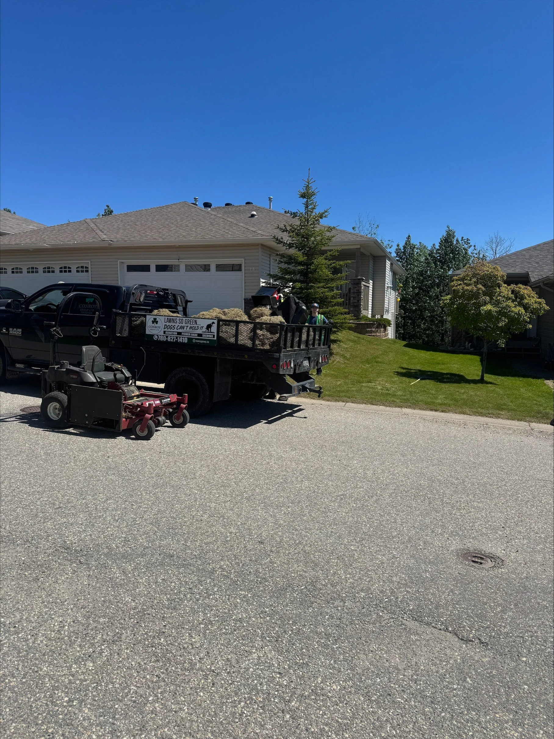 Front yard with a lawn and trees, house with a garage, and a pickup truck parked on the street with yard equipment in the bed of the truck.