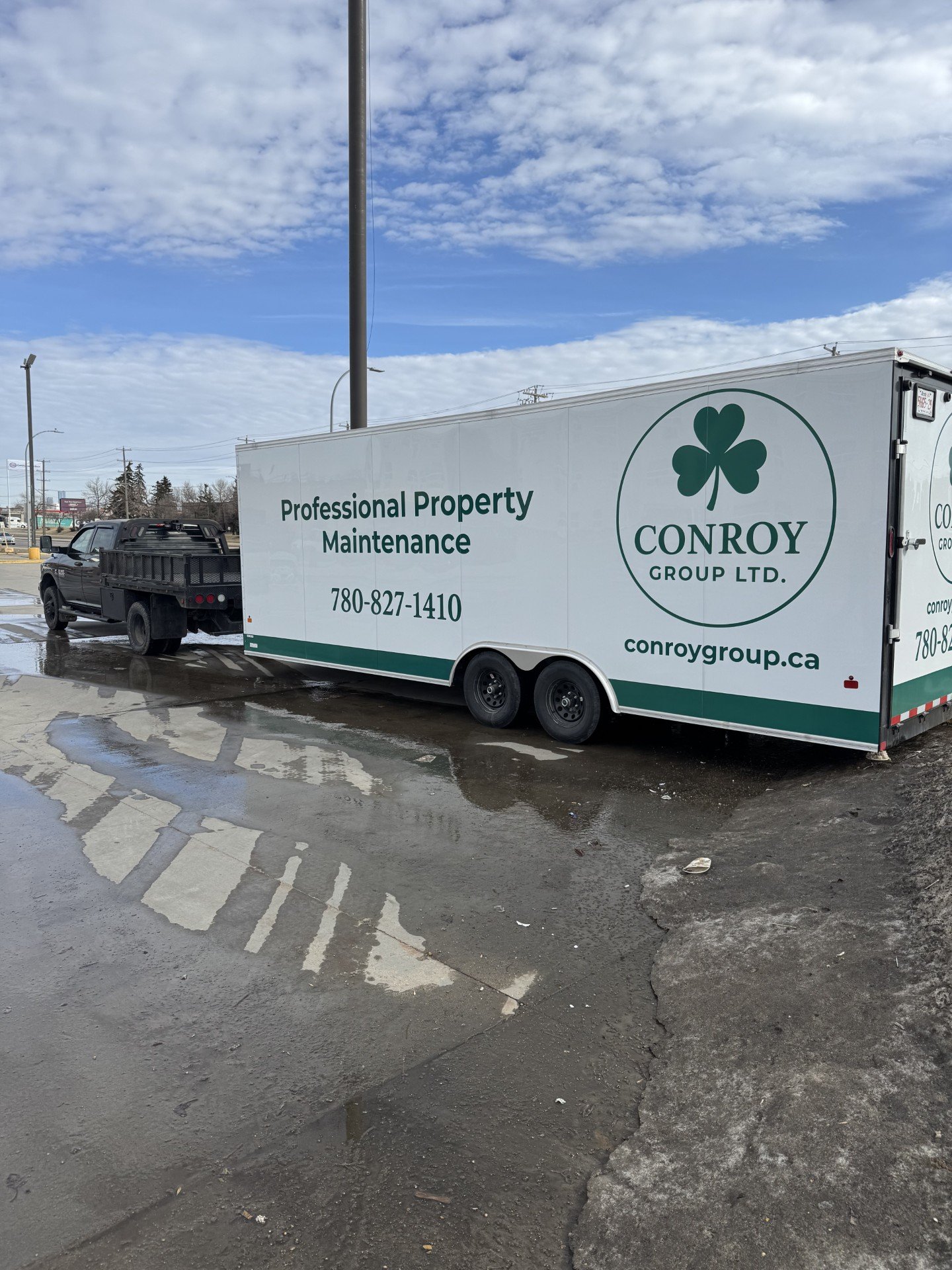 A moving truck belonging to Conroy Group Ltd. parked in a wet parking lot with some puddles and patches of ice. The truck has signage reading 'Professional Property Maintenance' along with contact information and a shamrock logo.
