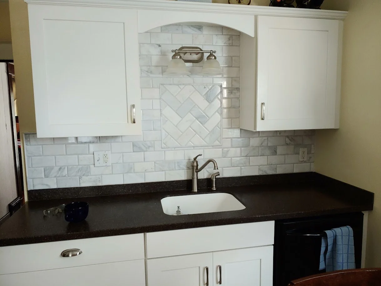 Kitchen with white cabinets, a dark countertop, a white sink, a silver faucet, white subway tile backsplash with decorative tile, and a black oven.