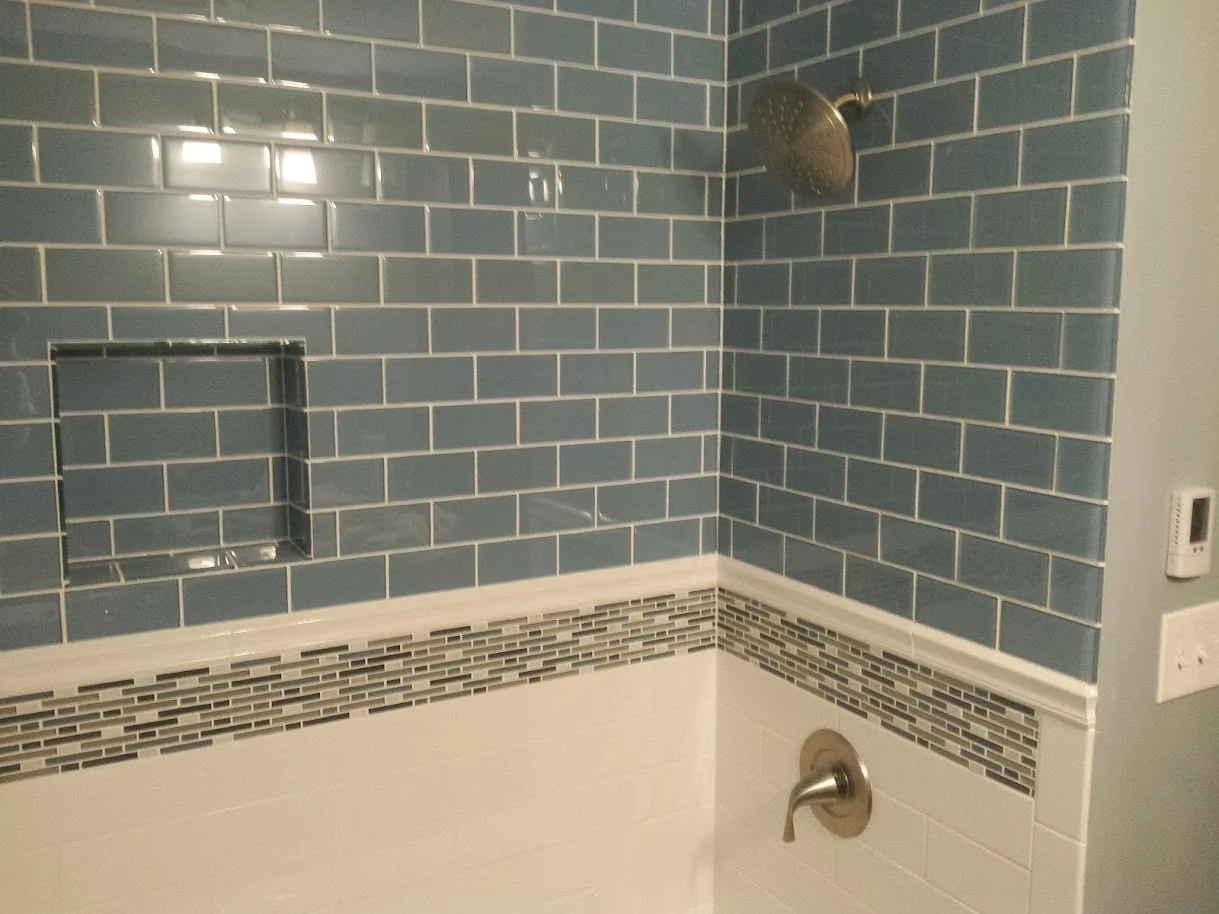 Bathroom shower with blue subway tiles, a built-in niche, a decorative mosaic border, and a brushed nickel showerhead and faucet.