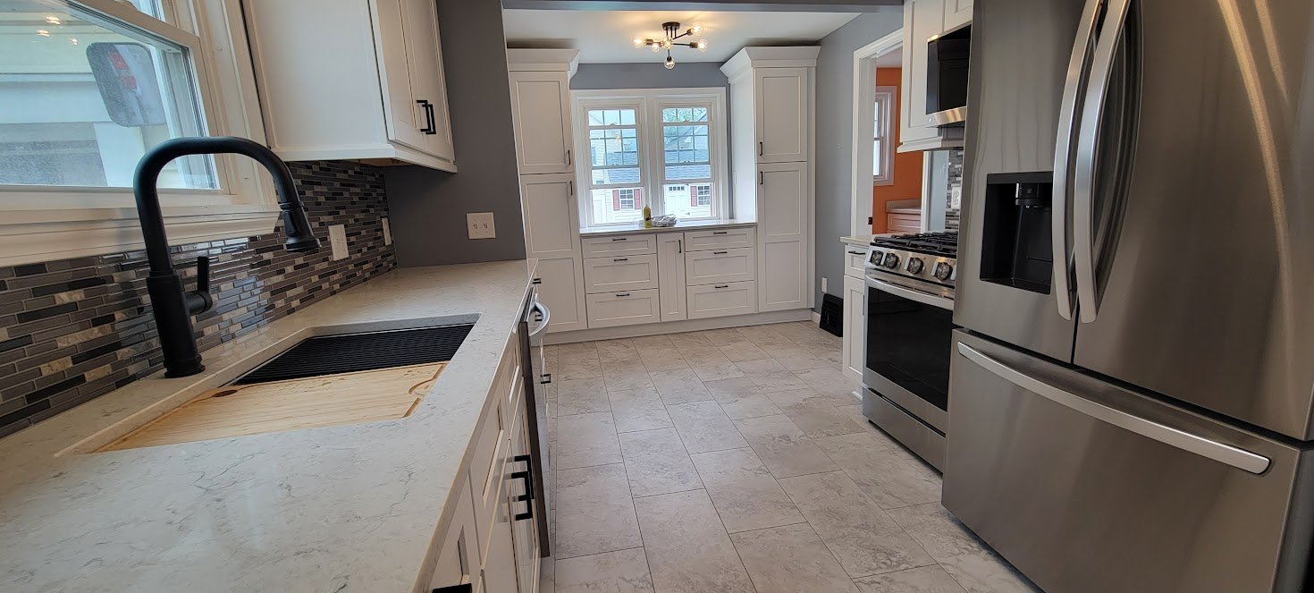 Modern kitchen with white cabinets, stainless steel appliances including a refrigerator and stove, a black sink with a black faucet, a window above the sink, tiled flooring, and a gray and mosaic backsplash.