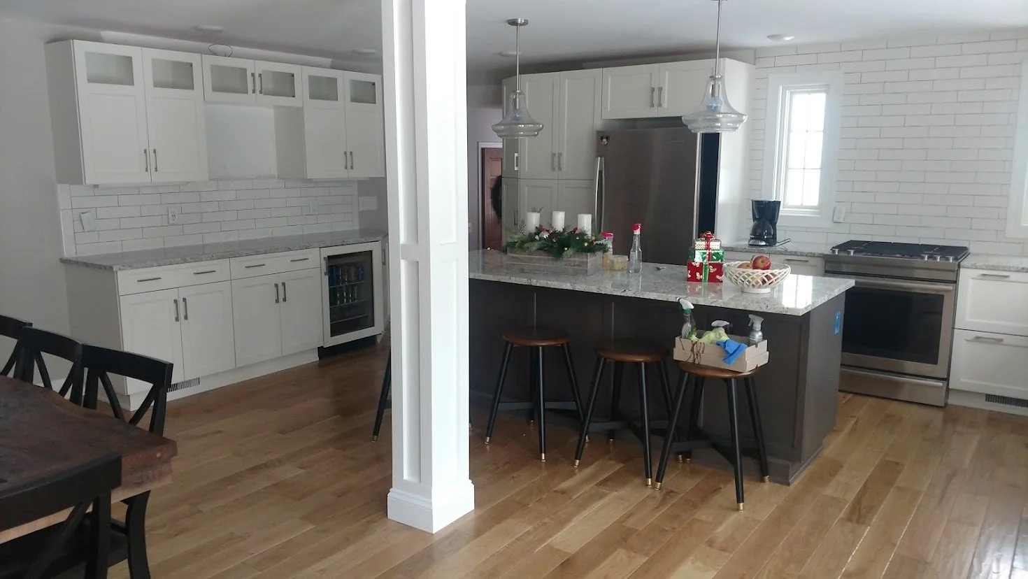 Modern kitchen with white cabinets, gray island with barstools, stainless steel appliances, white subway tile backsplash, hardwood floors, and holiday decorations on the island.