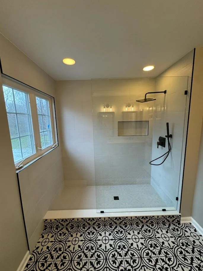Modern walk-in shower with a glass door, black fixtures, and patterned black-and-white floor tiles.