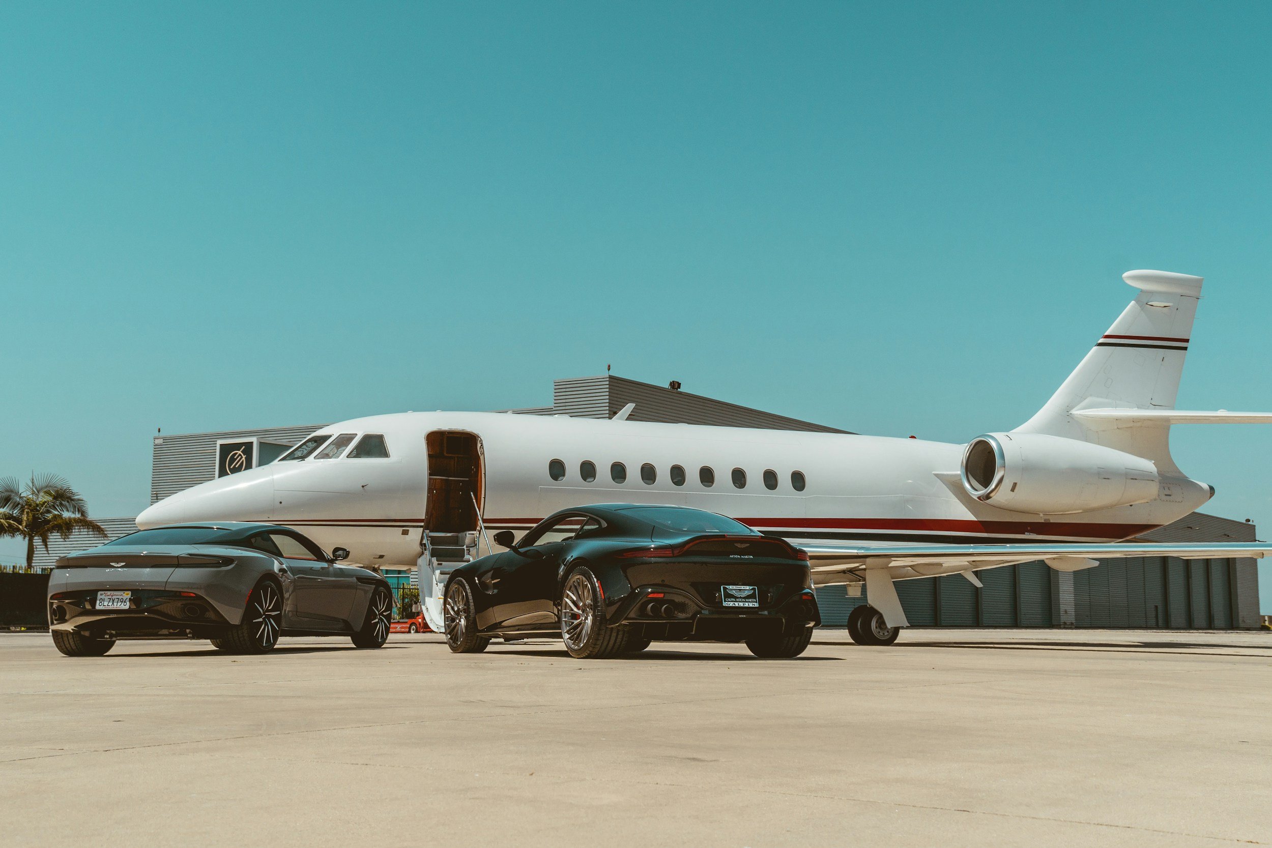Multiple black luxury cars parked under a private jet aircraft at an airport.