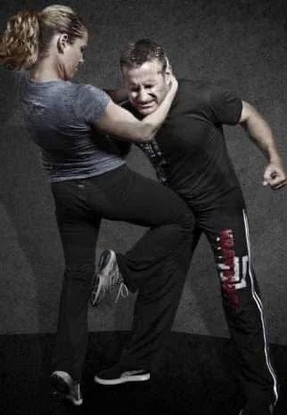 A woman is practicing self-defense or martial arts against a man, blocking his punch with her arm while he is in a punching stance.