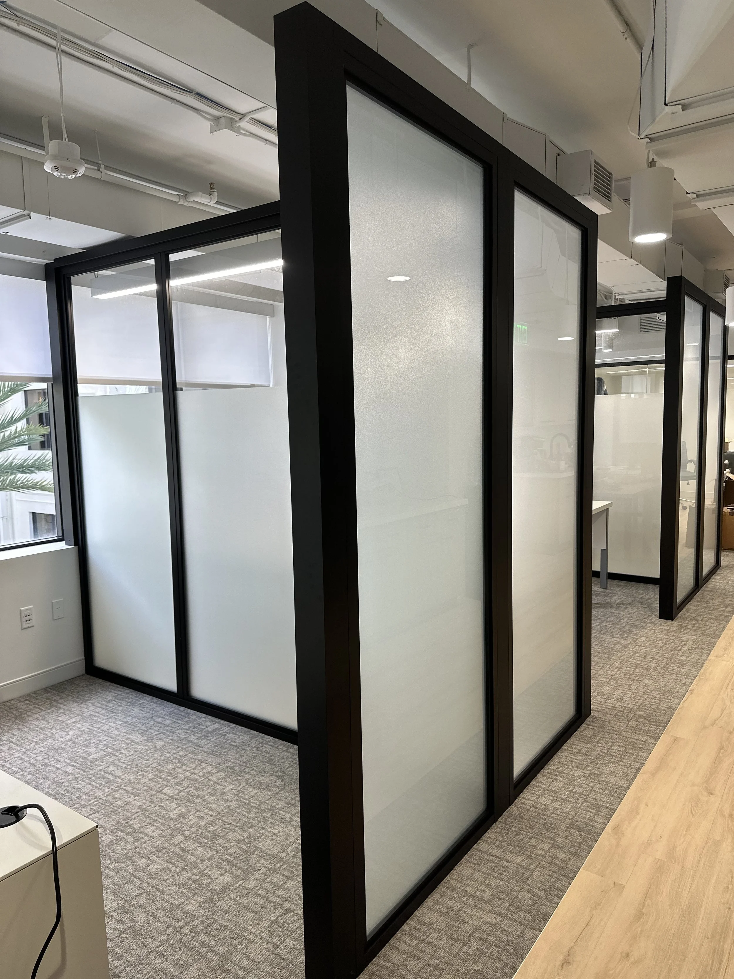 Office space with glass partition walls, some with frosted glass for privacy, and exposed ceiling with lighting fixtures.