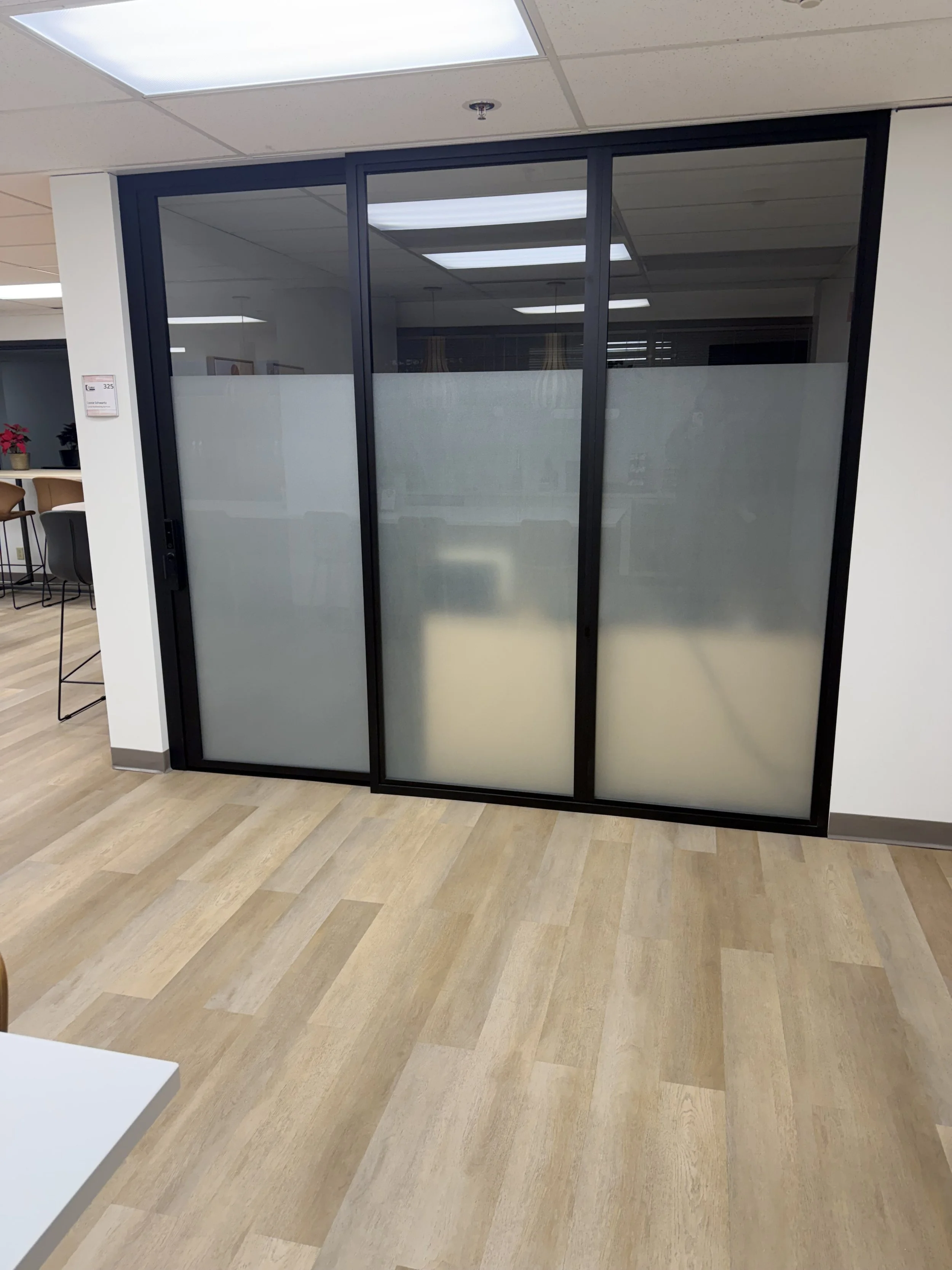 A black-framed glass sliding door with frosted bottom panels leading into an office.