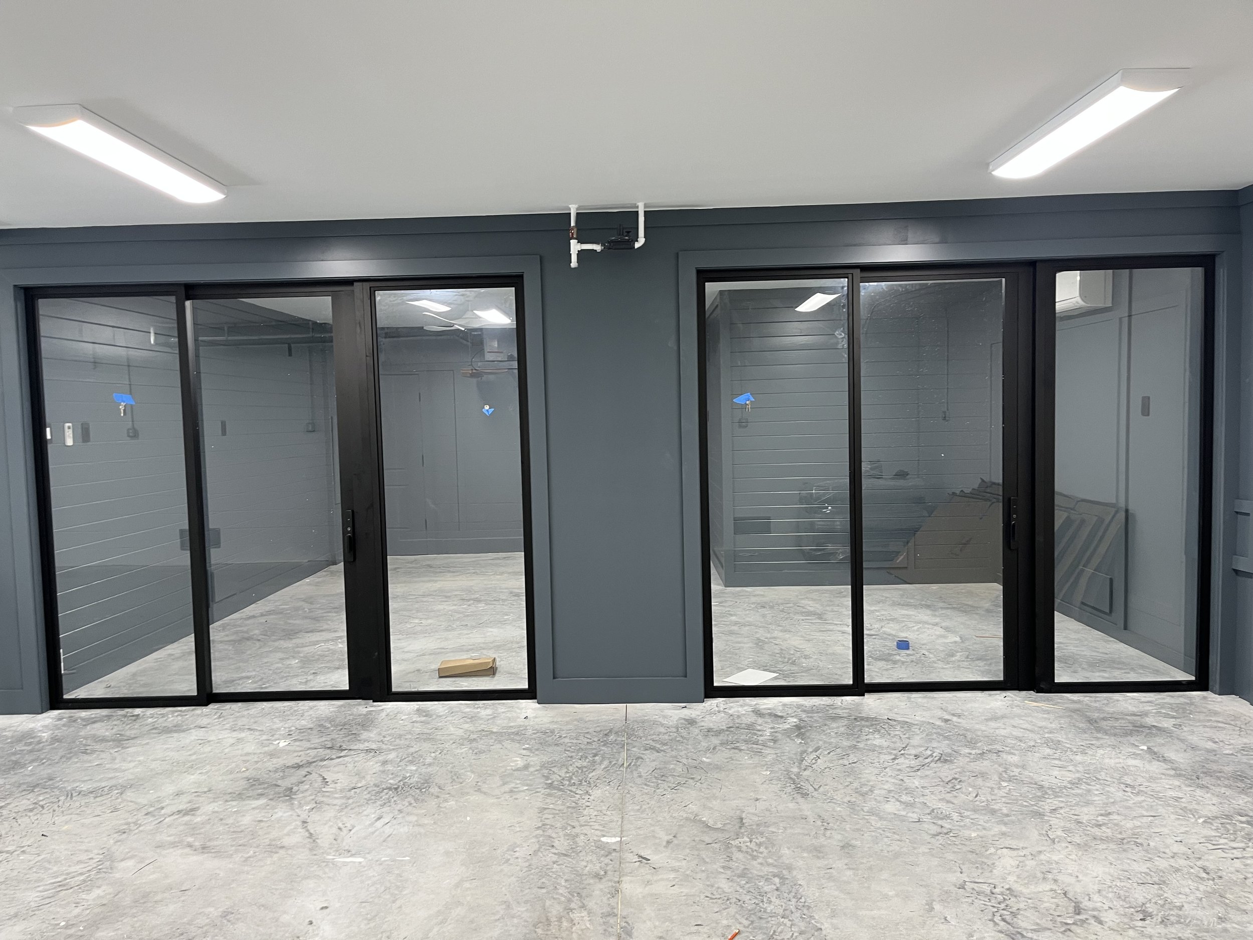 Interior space with large glass sliding doors and blue-gray walls, with emergency lighting and ceiling fixtures, and concrete floor.