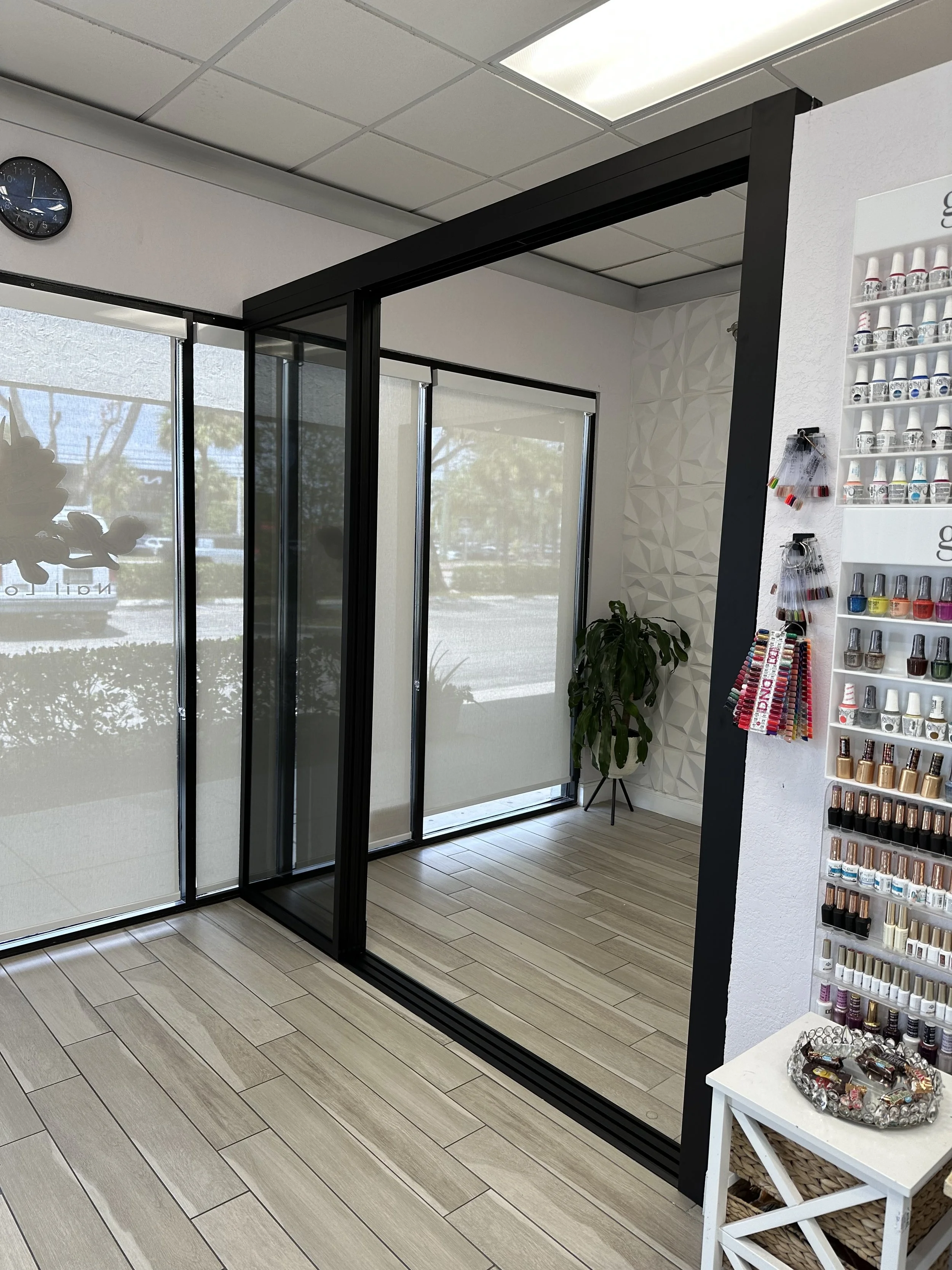 Empty nail salon in daytime with glass doors, nail polish display, and a green potted plant