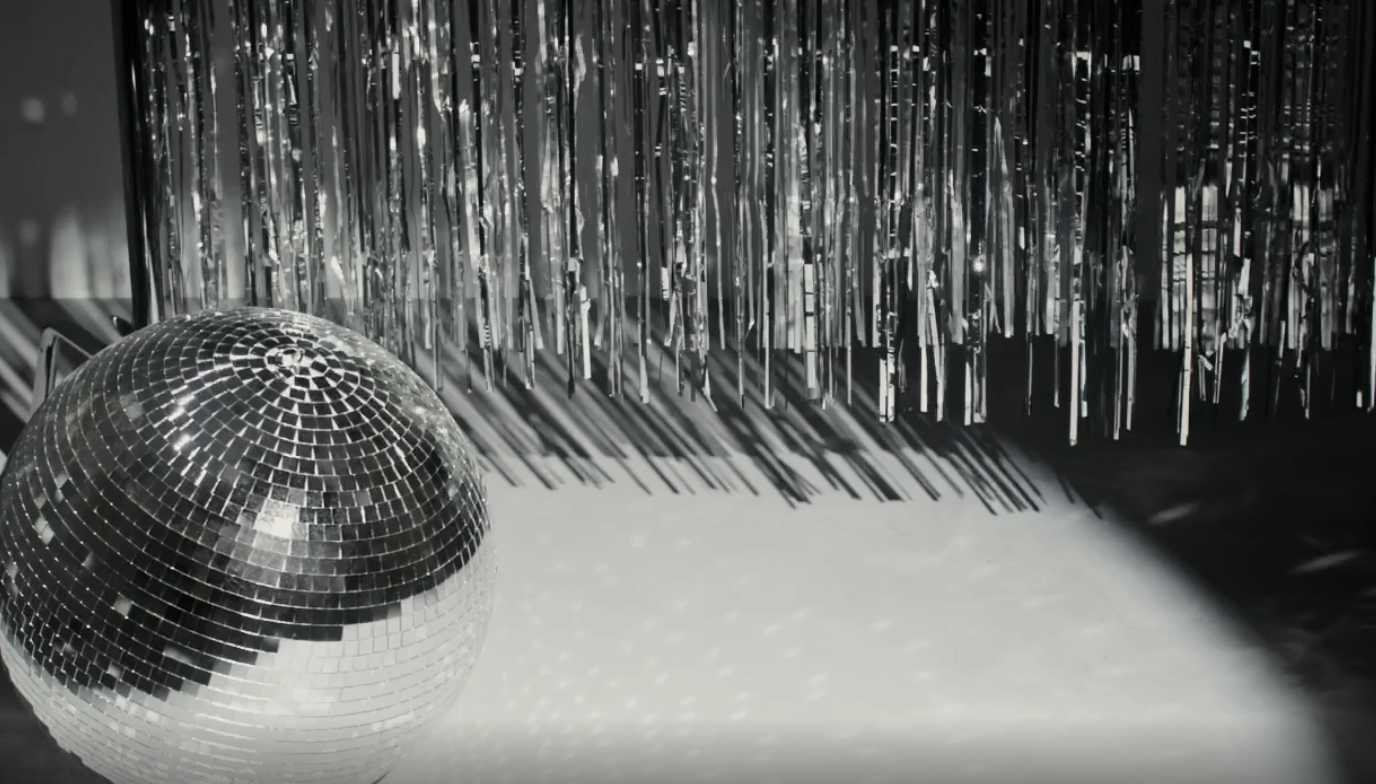 ein Spotlicht strahlt auf eine Discokugel und einen silbernen glänzenden Lamettavorhang an. Beides bewegt sich etwas und glitzert und glänzt im Licht.