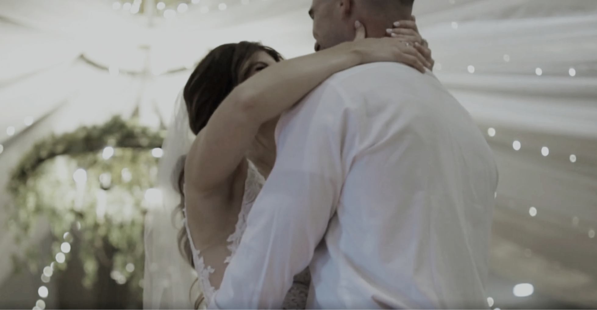 Ein Brautpaar umarmt sich auf einer Hochzeit im Freien unter einem weißen Zelt mit Lichterketten. Sie sehen sehr glücklich aus.