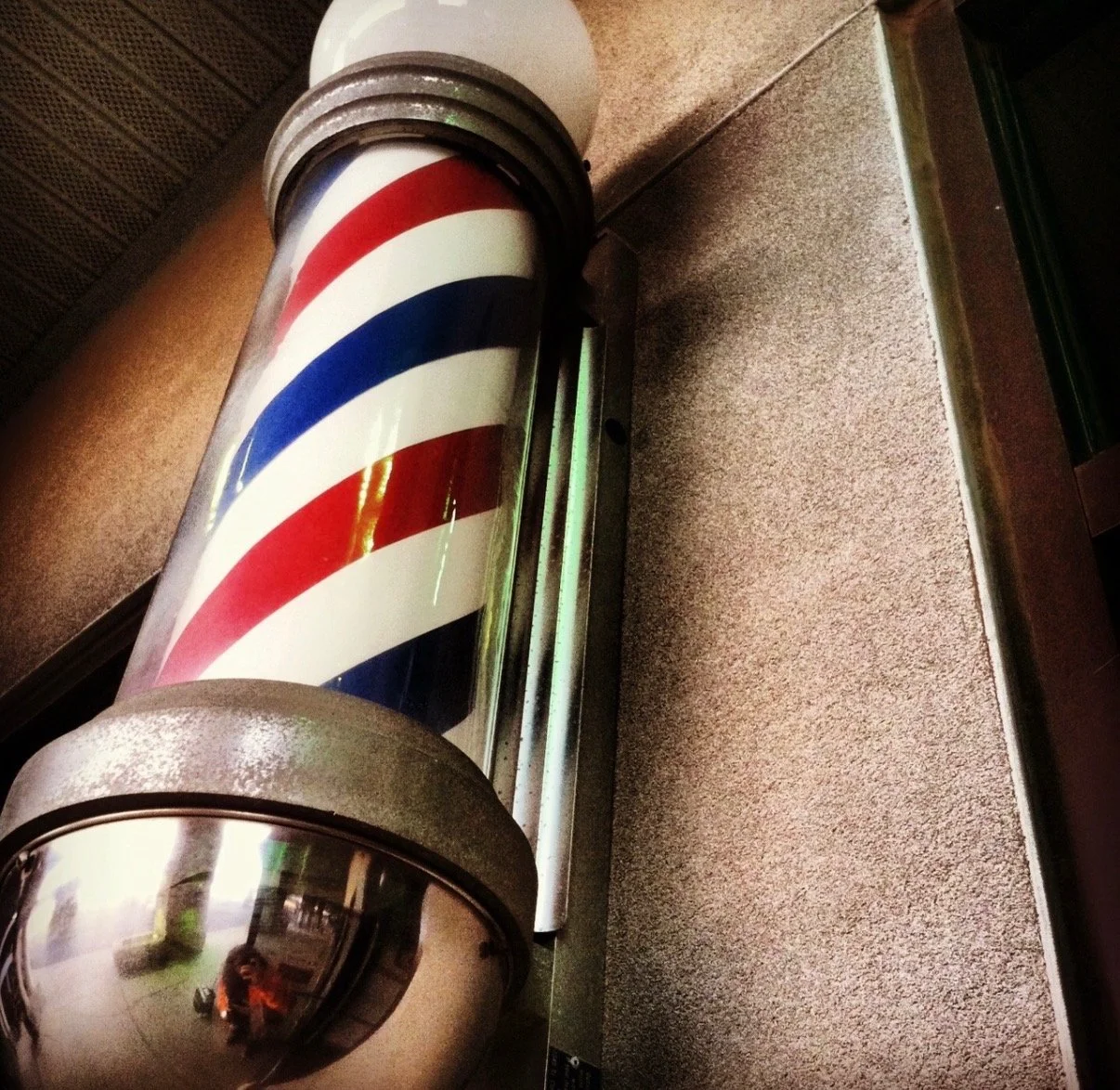Close-up of a vintage barber pole with red, white, and blue stripes, mounted on a textured wall.