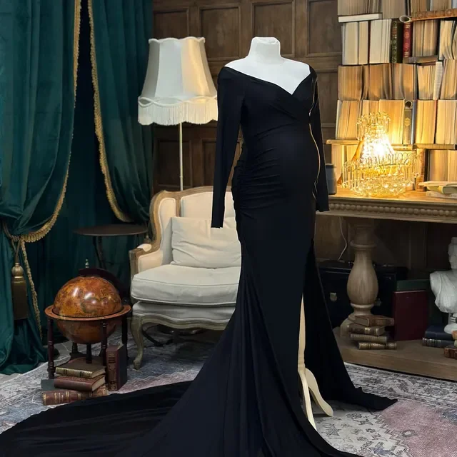 Schwarzes glamouröses Abendkleid auf einem Dummy in einem eleganten Raum mit Bücherregal, Sessel, Stehlampe und Deko-Elementen.