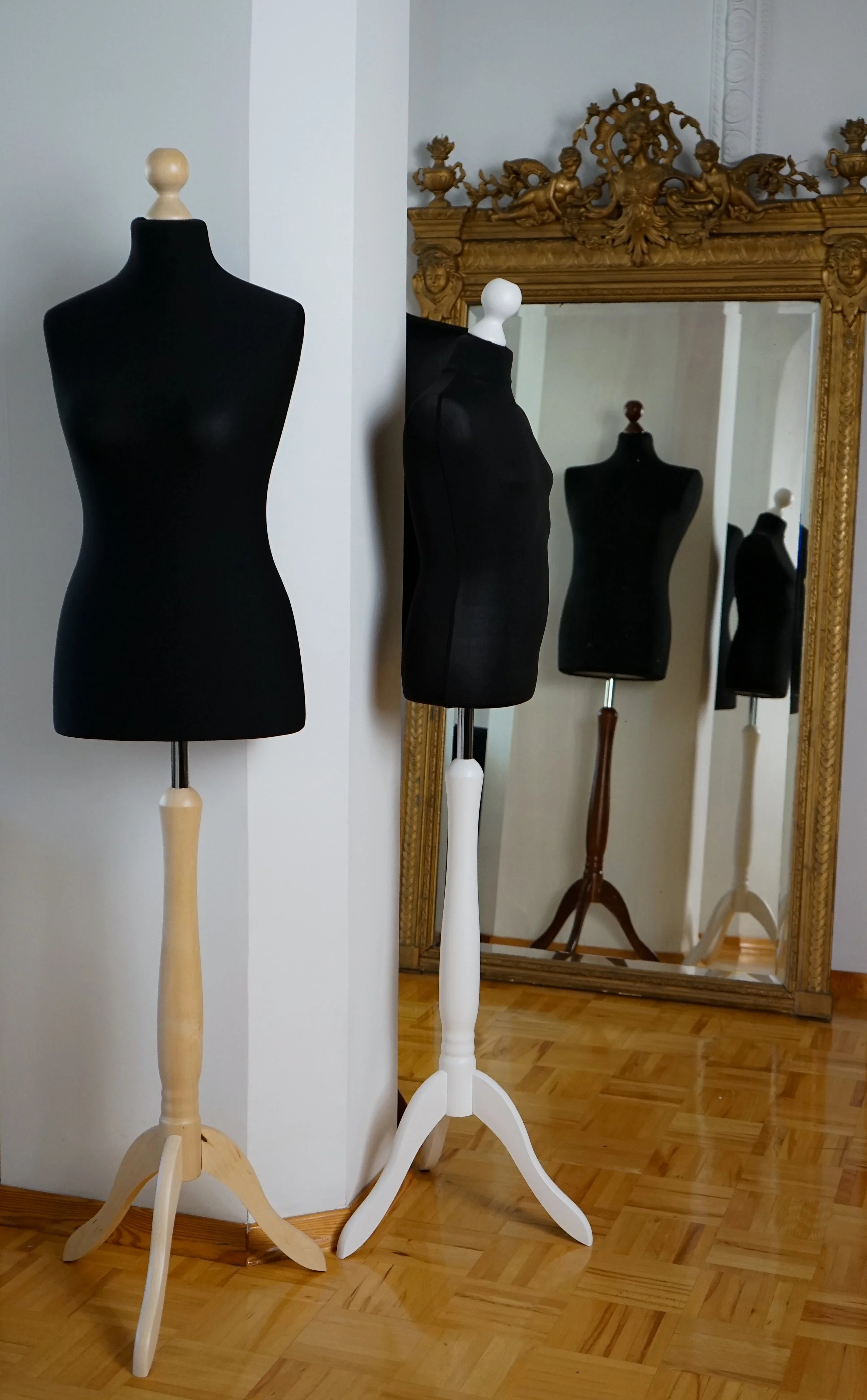 Drei Kleiderpuppen auf Holzständern vor einem großen, antiken goldfarbenen Spiegel.