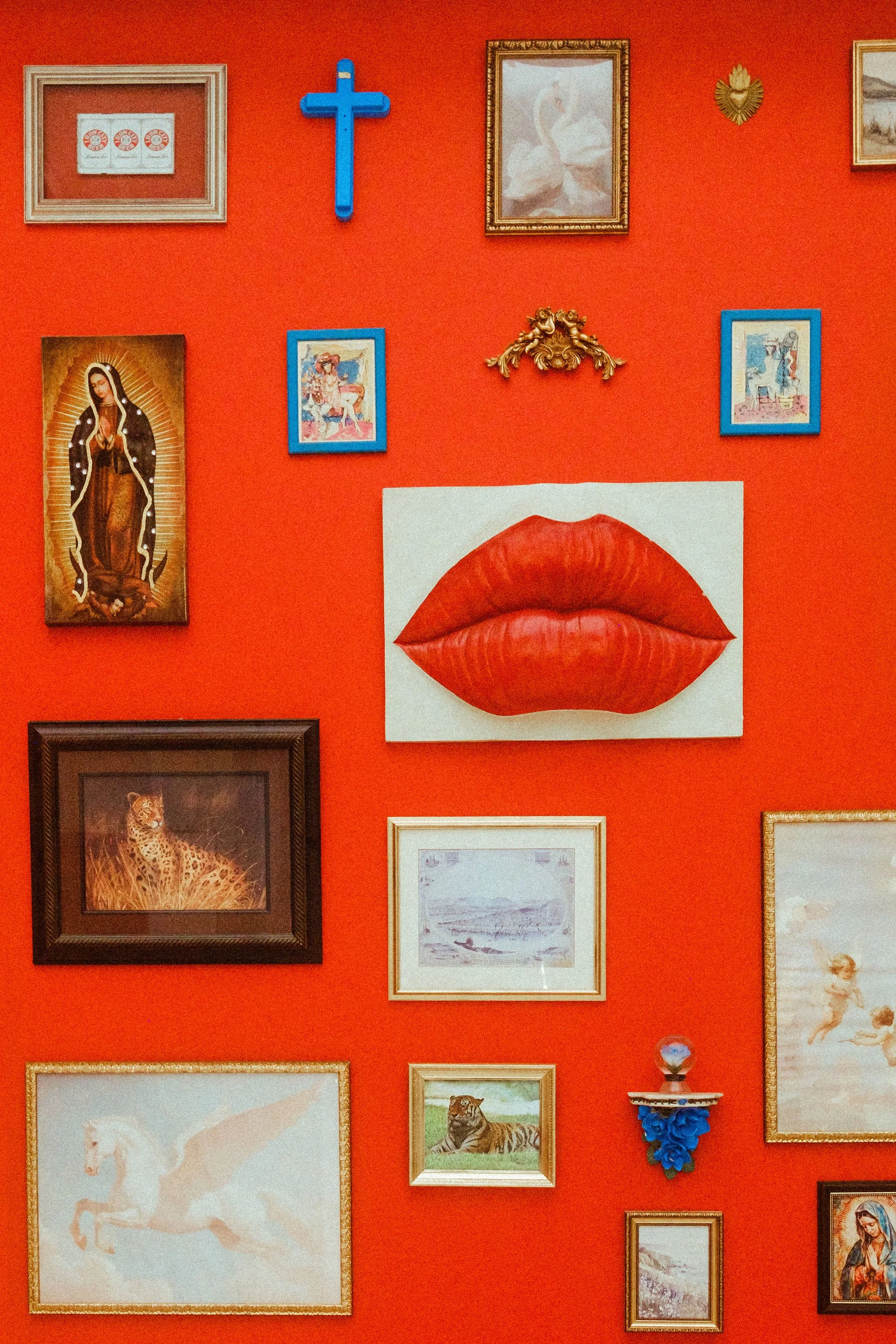 A wall with a variety of framed pictures and decorative items, including religious images, animals, and art, set against a red background.