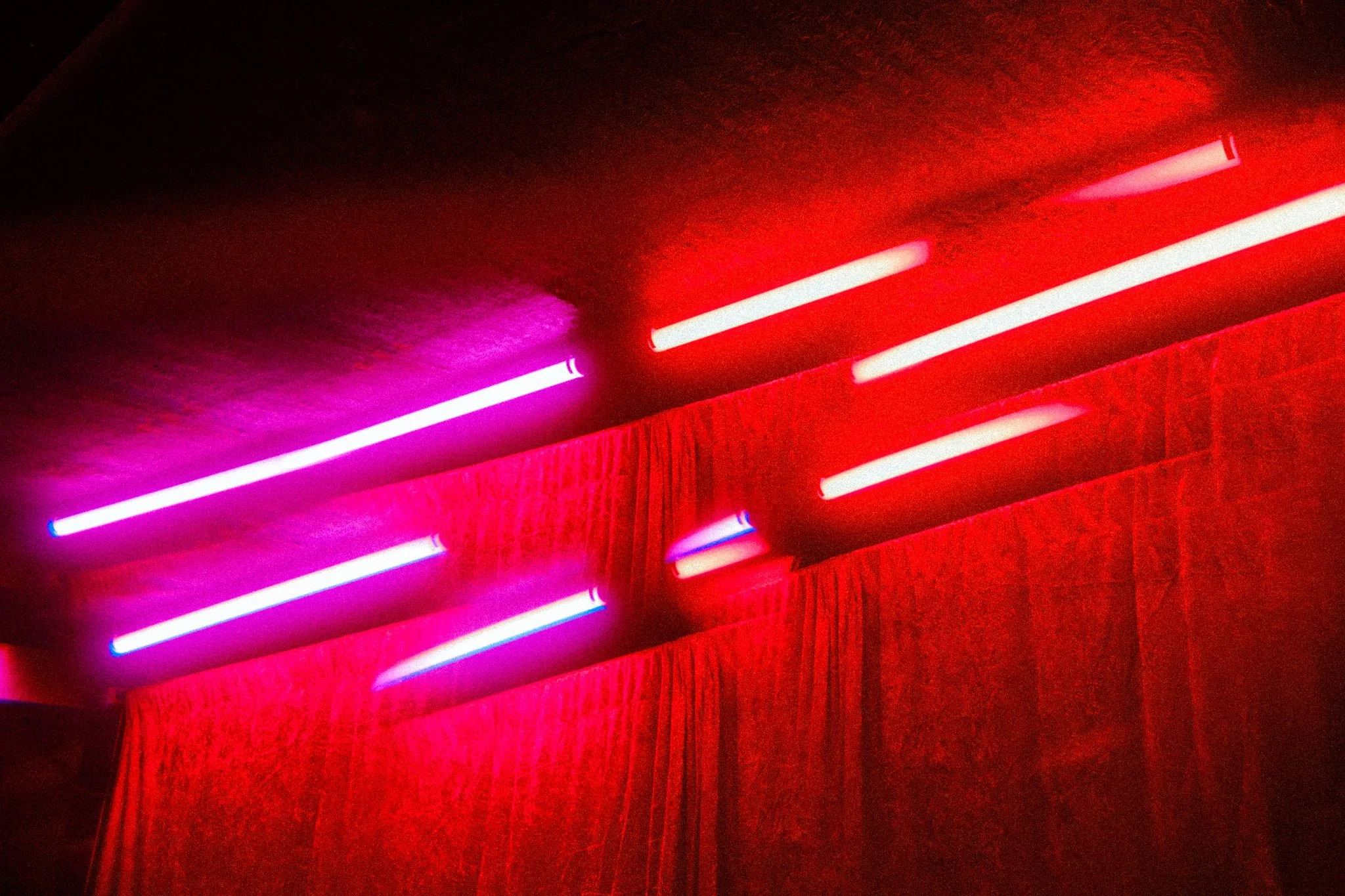 Neon lights in pink, red, white, and purple colors illuminating on a textured ceiling and a red curtain.