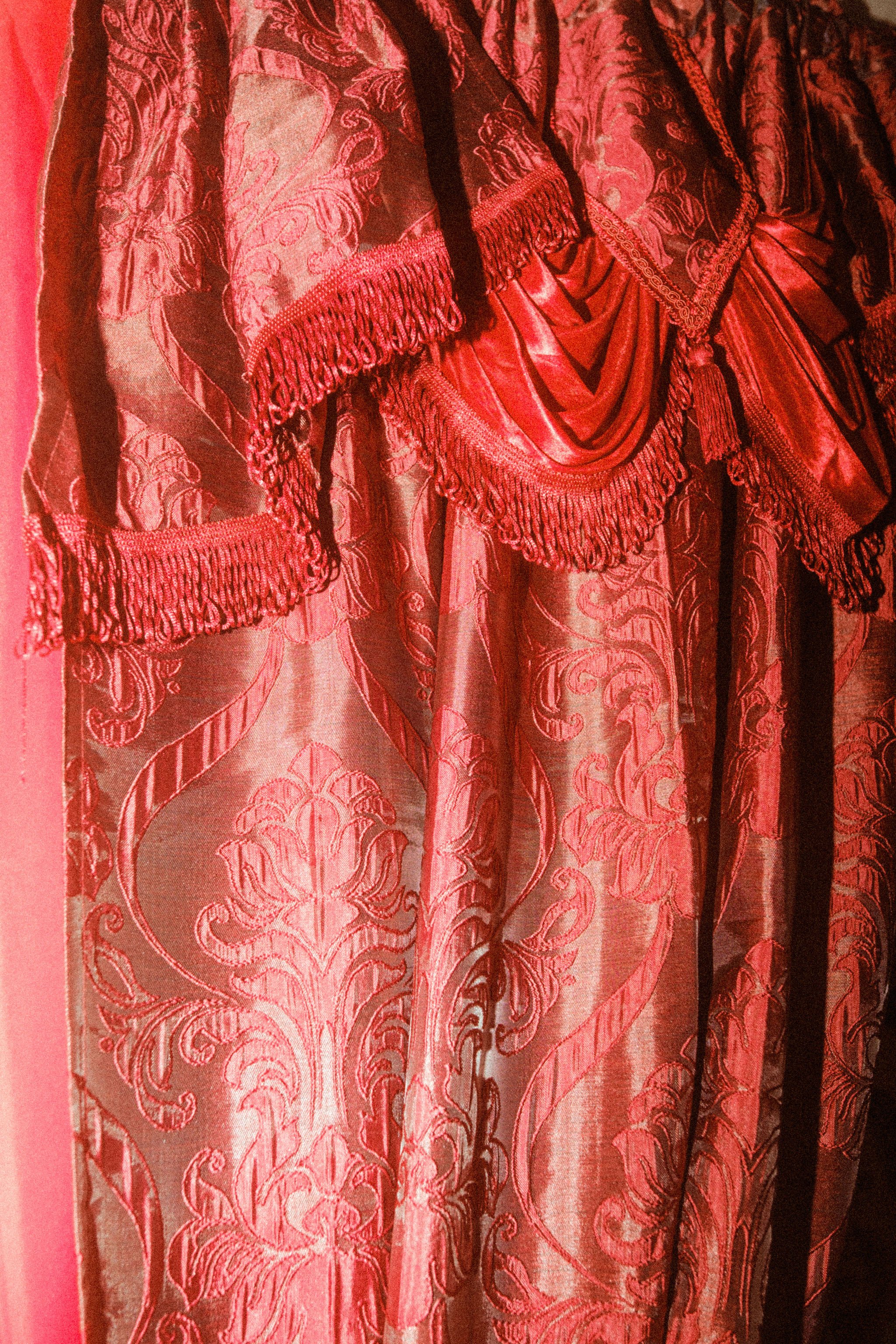 Close-up of a fabric with intricate floral patterns and fringes, primarily in shades of red and pink.