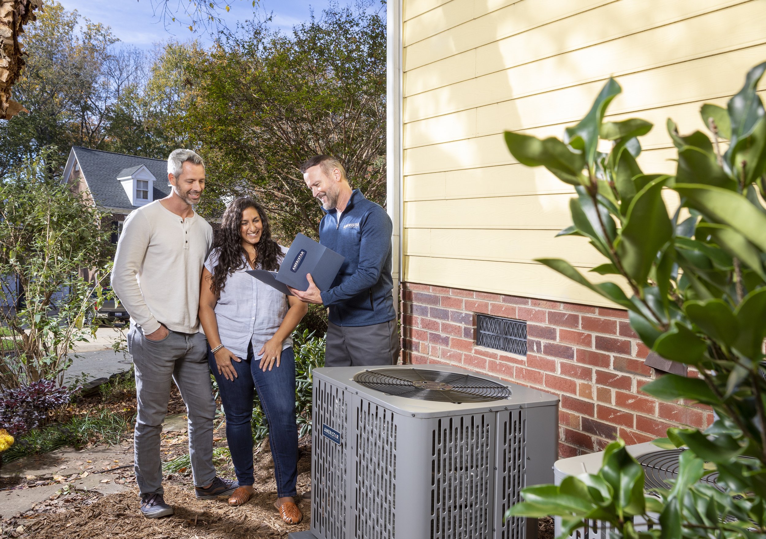 Homeowners reviewing their new American Standard air conditioner with an HVAC professional outside their home.