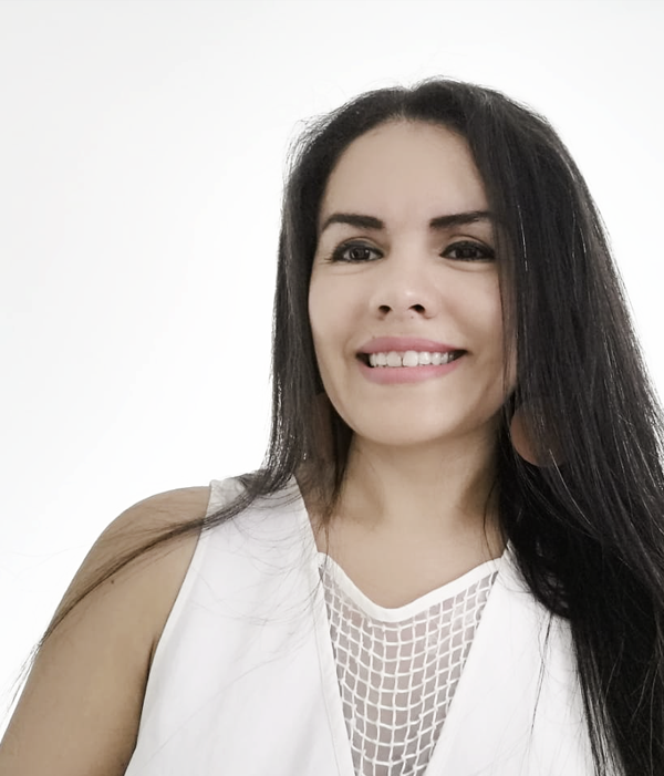A smiling woman with long dark hair wearing a white sleeveless top with a mesh detail, standing against a plain white background.