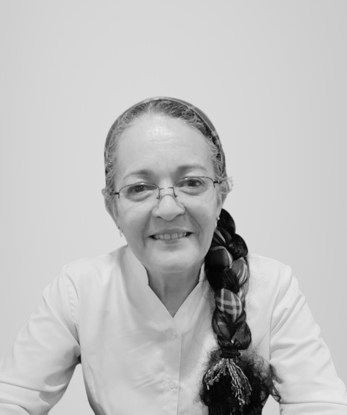 A smiling woman with glasses and a braid, wearing a white coat, against a plain background.