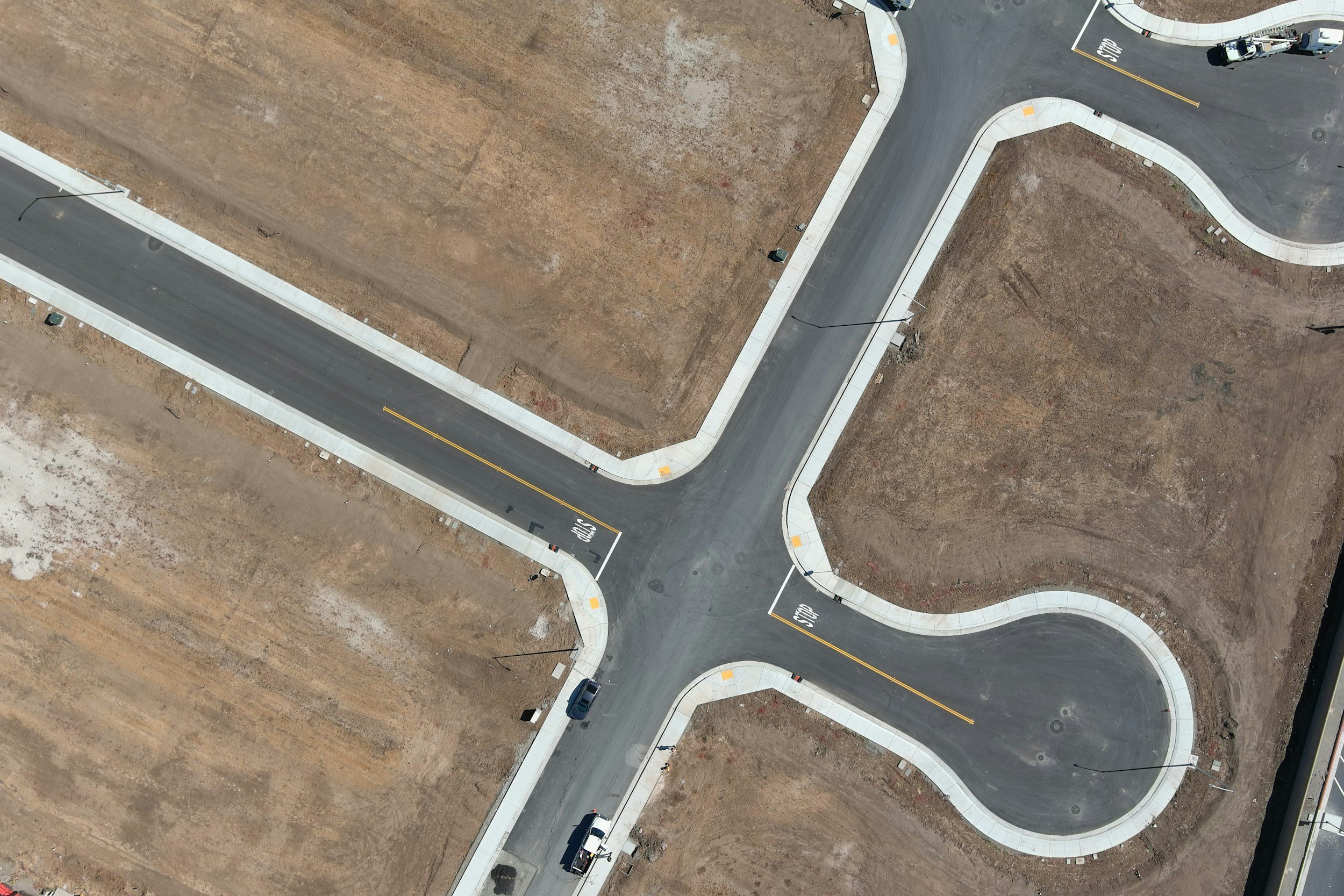 An aerial view of newly paved roads and curbs in a developing neighborhood, with some construction equipment and vehicles present.
