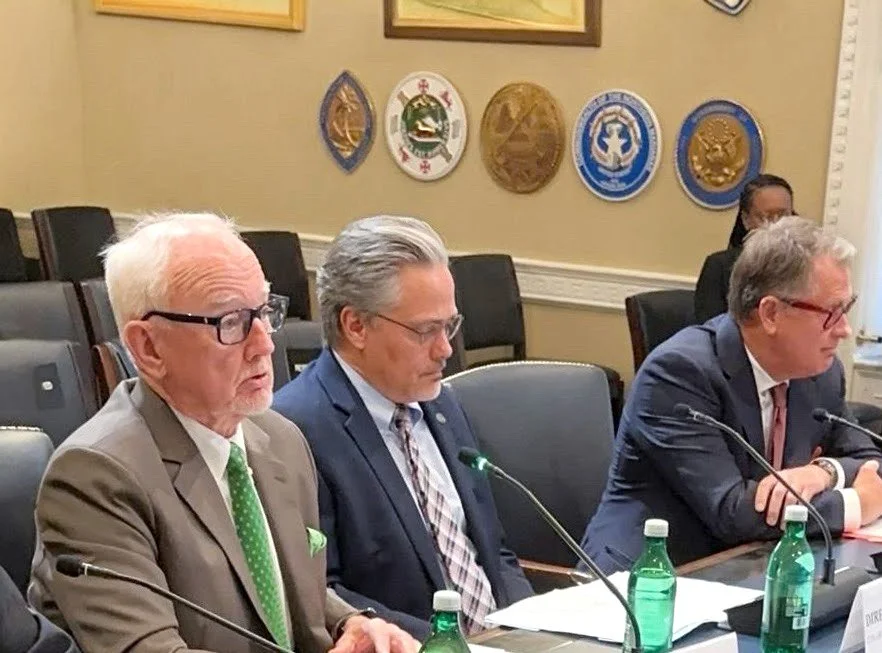 George Bray for McCracken County Judge Executive Kentucky and two men sitting at a conference table with microphones and bottled water, in a room with framed emblems or plaques on the wall.