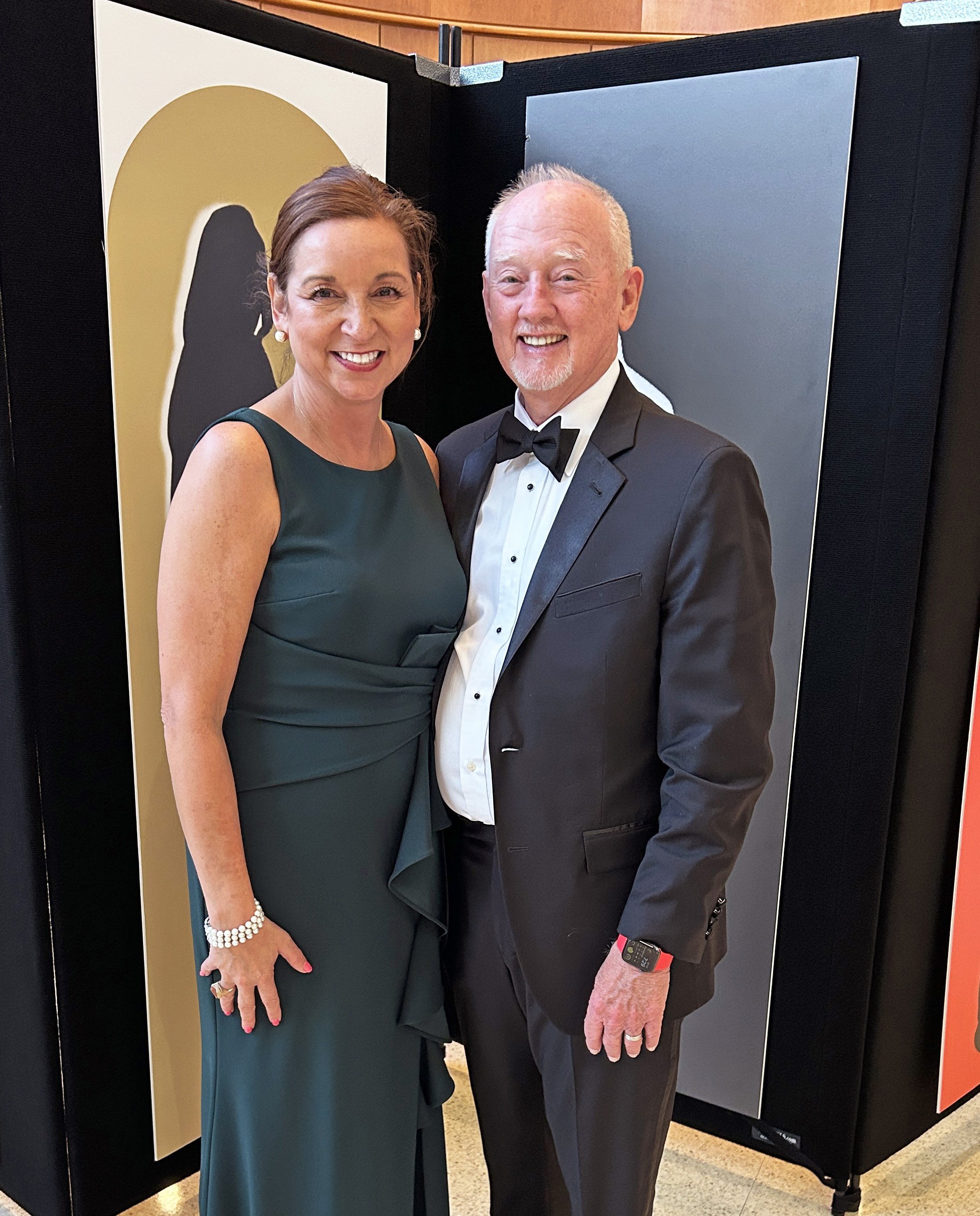 George Bray for McCracken County Judge Executive Kentucky and wife, Angela, smiling and standing close together at an event. They are behind a black display board with various colored panels.