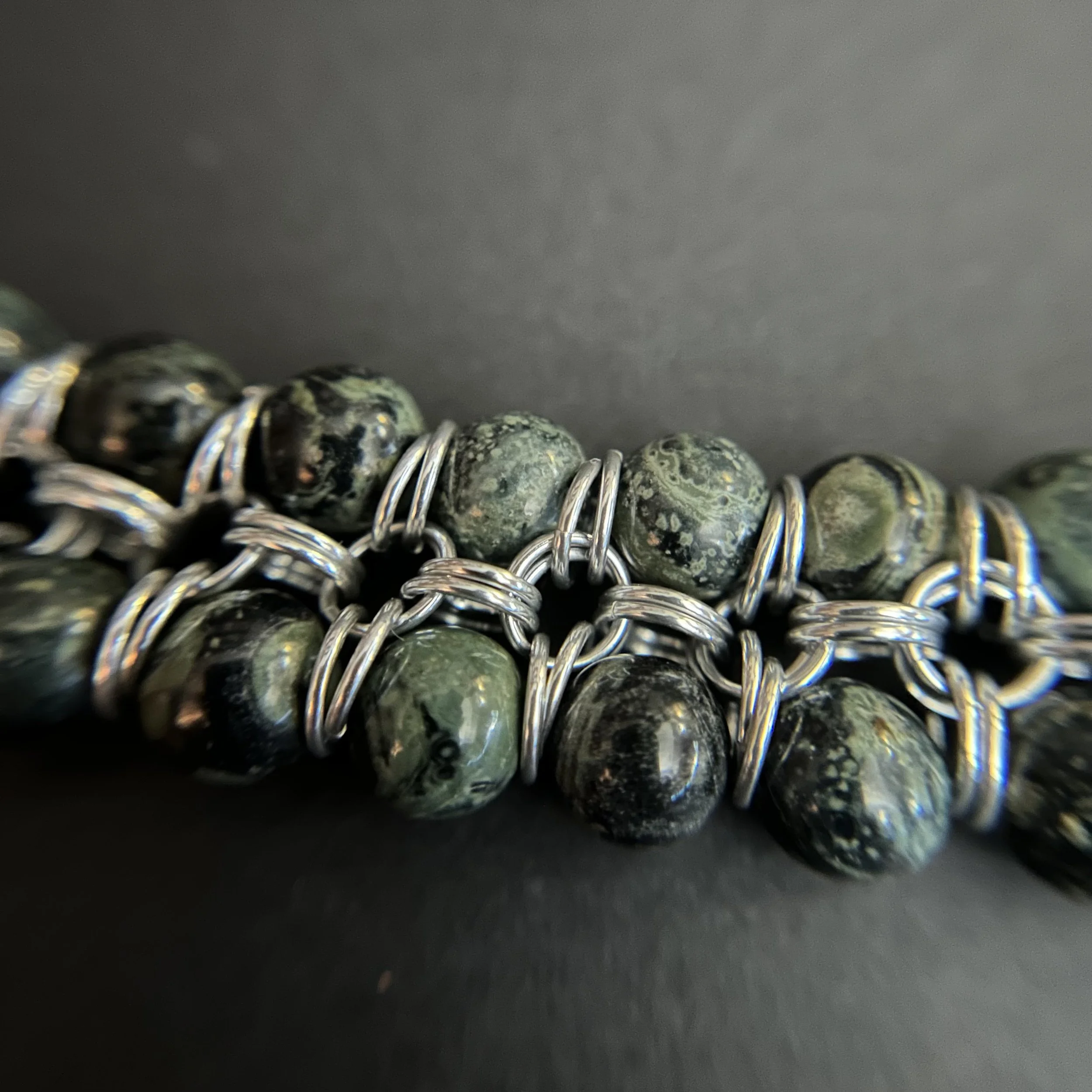 Closeup of Kambaba Jasper beads connected by bright silver aluminum rings in a twinstrand chainmaille pattern.