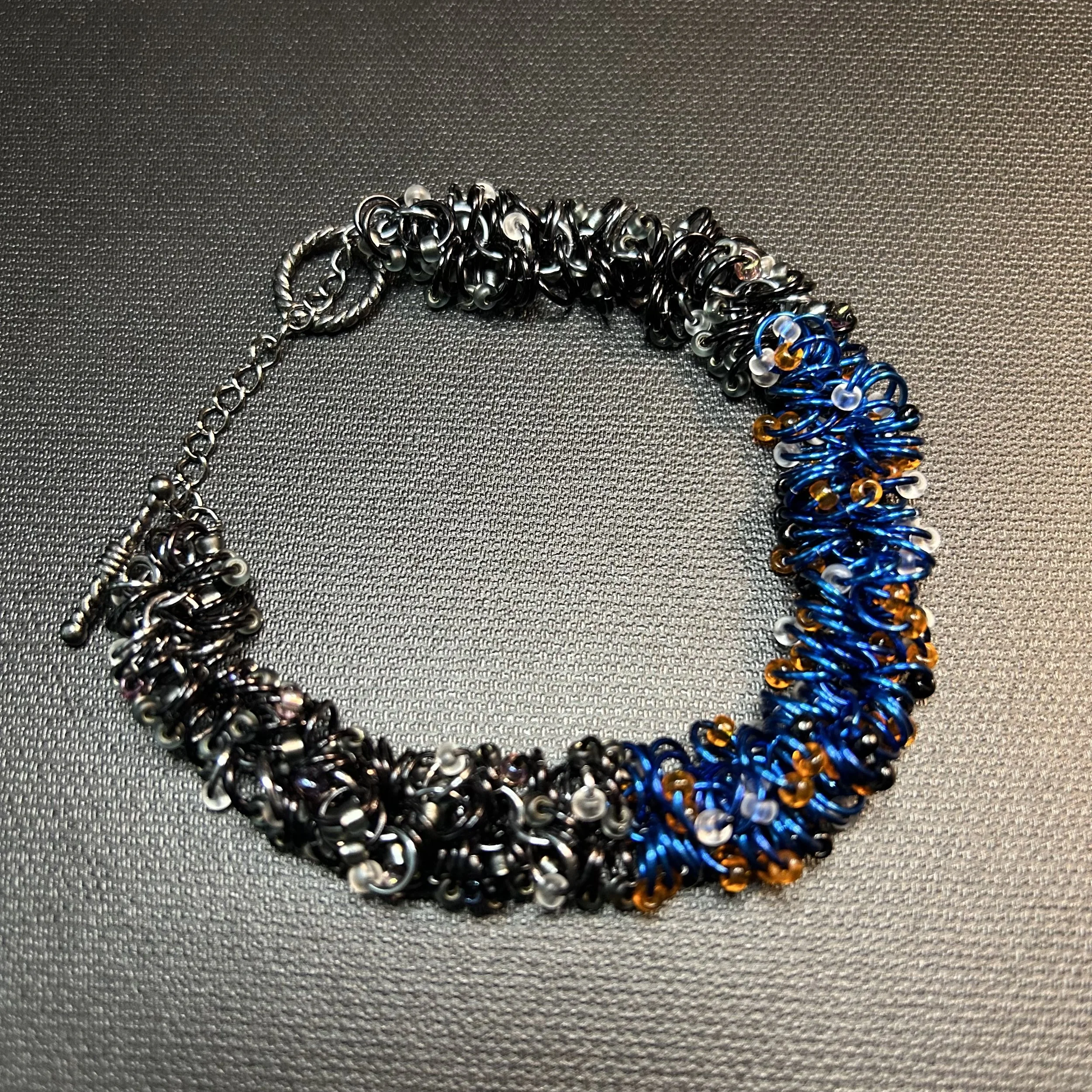 A flat‑laid shaggy‑loop bracelet showing its full gradient from black to Black Ice to royal blue, highlighting the thick six‑shag texture and gunmetal toggle clasp.