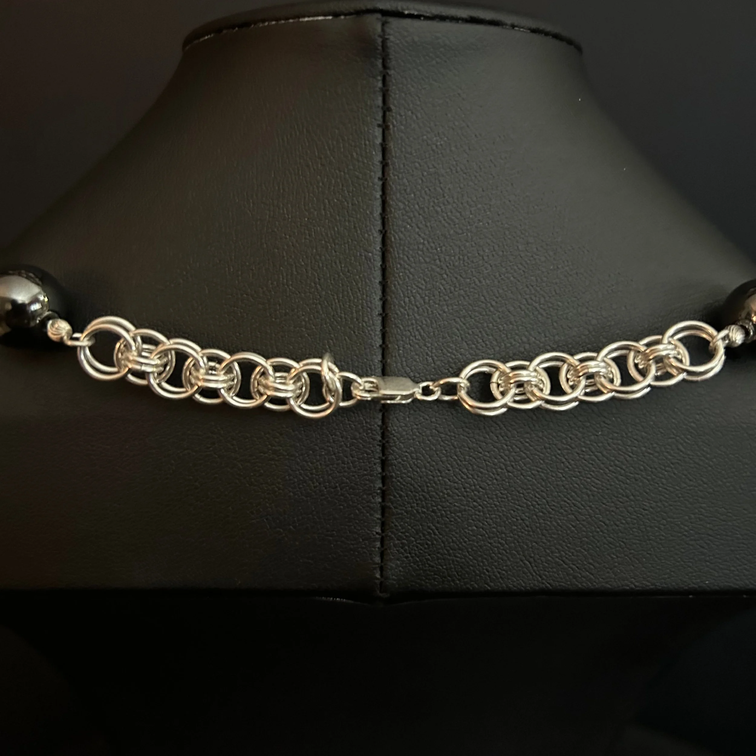 Close-up of the Silver Orbit necklace showing the sterling helm weave and central clasp framed by hematite beads