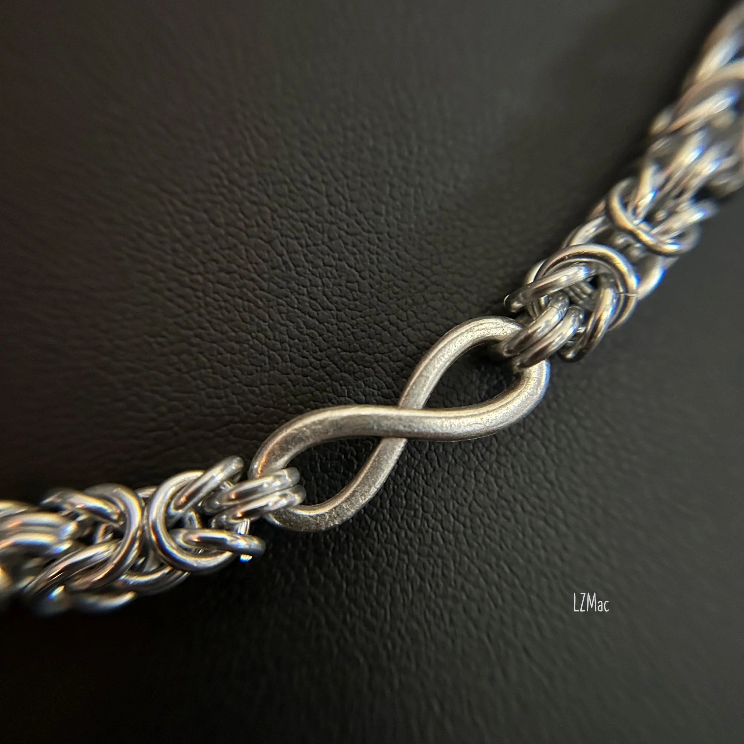 Close-up detail of the Silver Infinity necklace highlighting handwoven Byzantine chainmaille texture and matte silver infinity connectors.