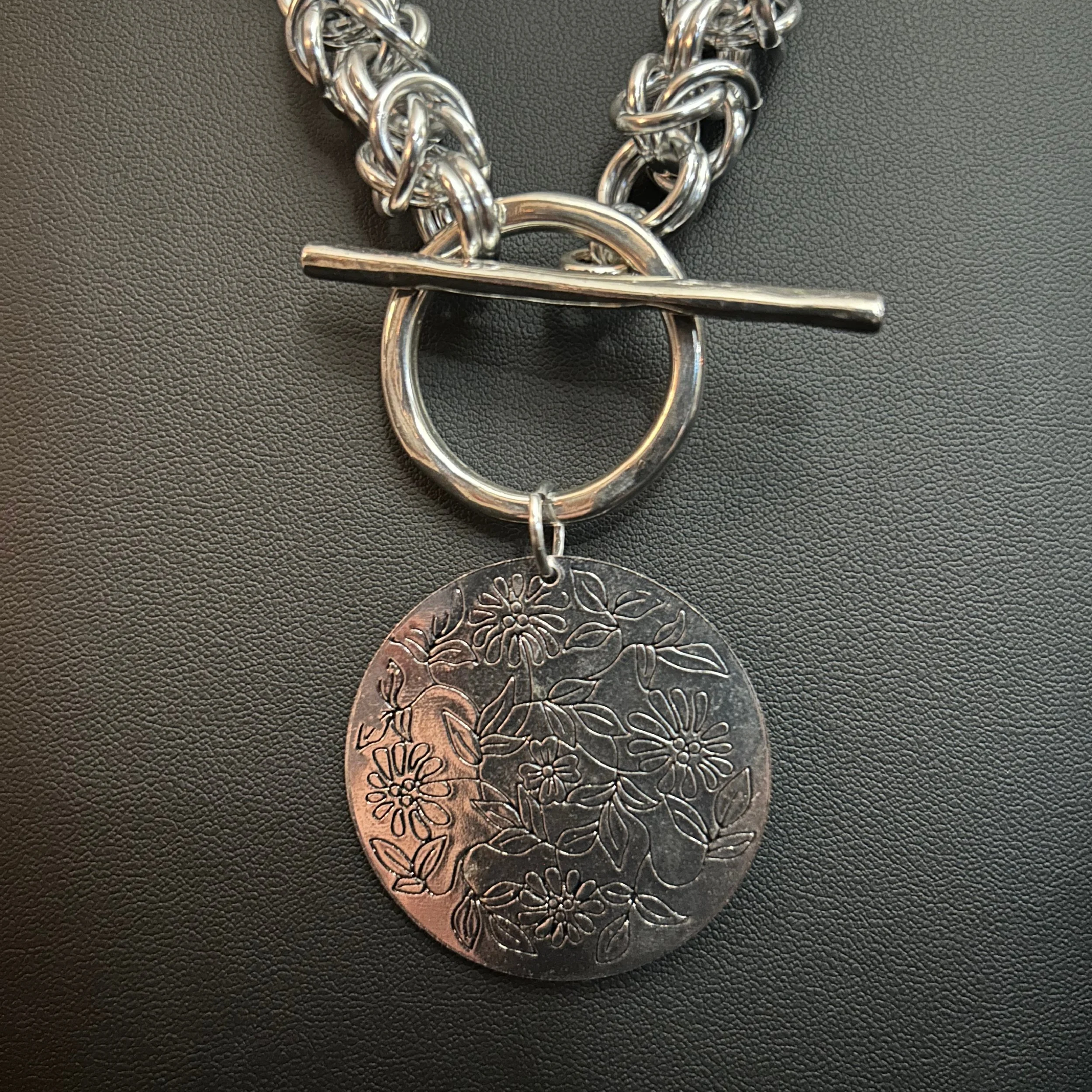 “Close-up of the silver floral focal and toggle clasp on the aluminum chain.”