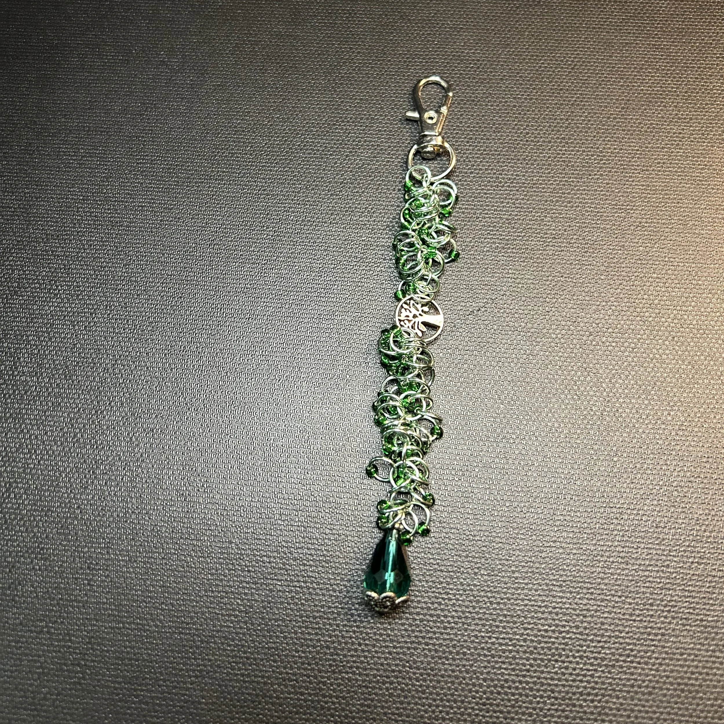 Green chainmaille purse charm shown flat on a dark surface with Tree of Life connector and green drop charm.