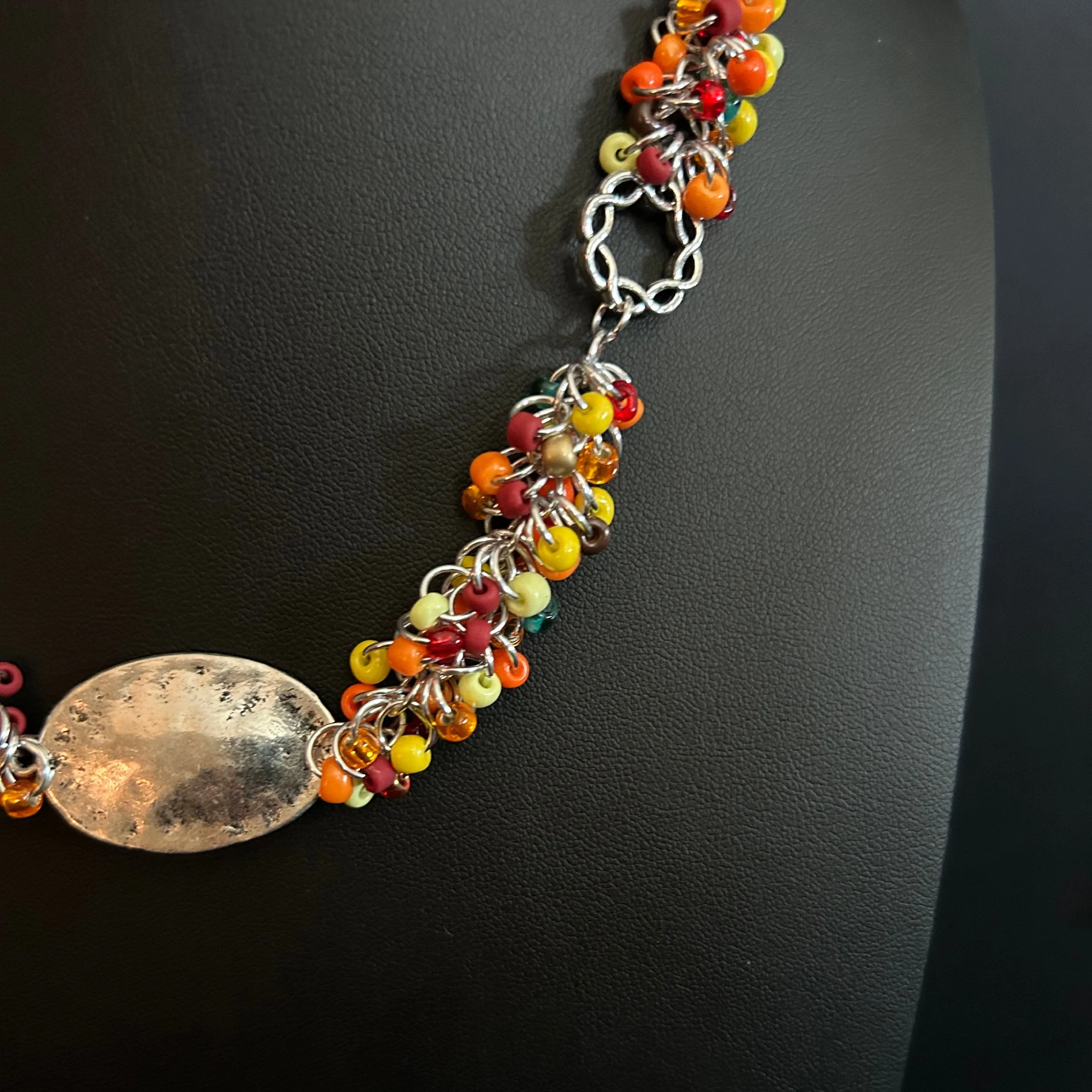 “Detail of the shaggy‑loop weave with red, orange, yellow, and green beads and the hammered connector.”