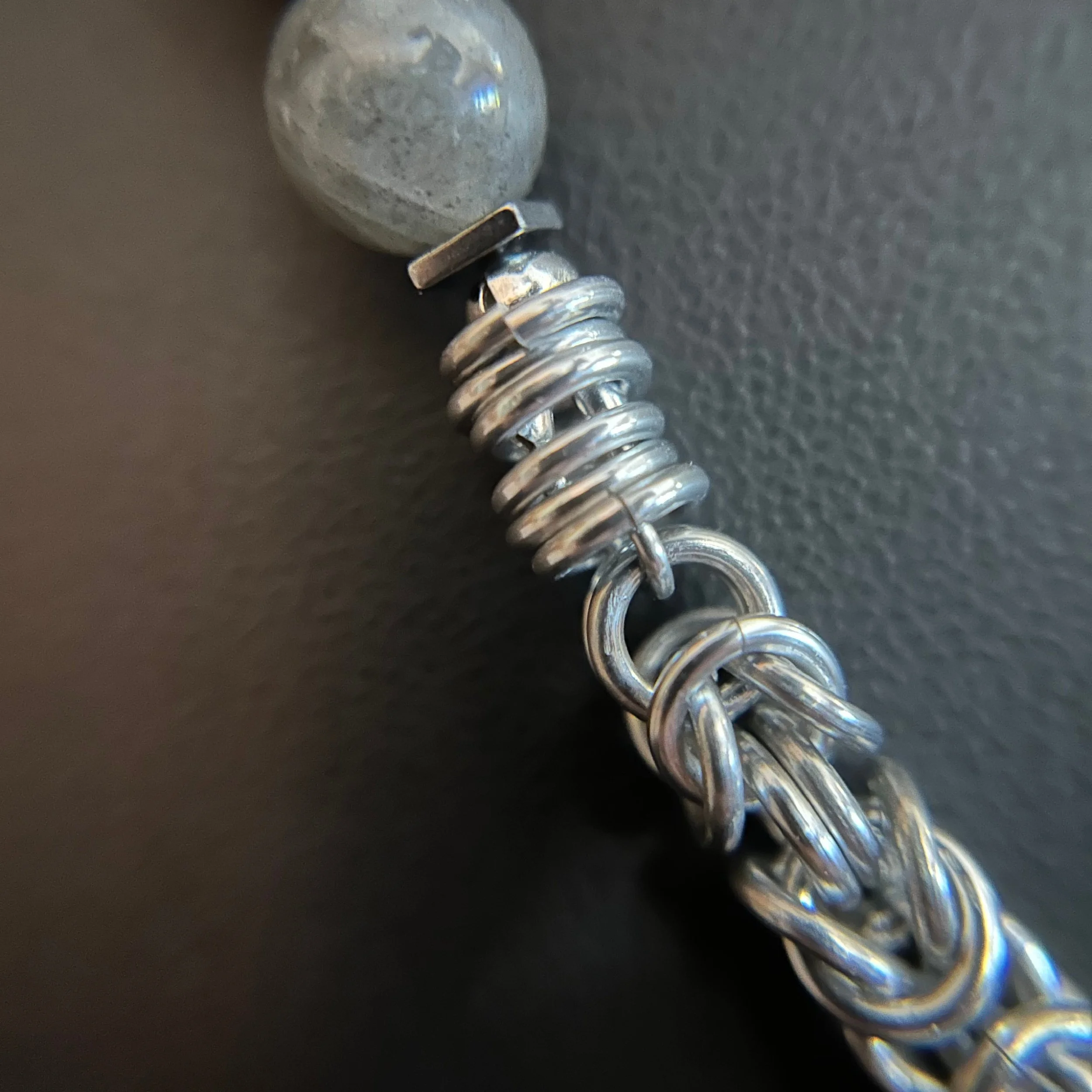 Close-up of the Moonline necklace showing a labradorite bead above a tightly wrapped silver coil and interlinked chainmaille rings