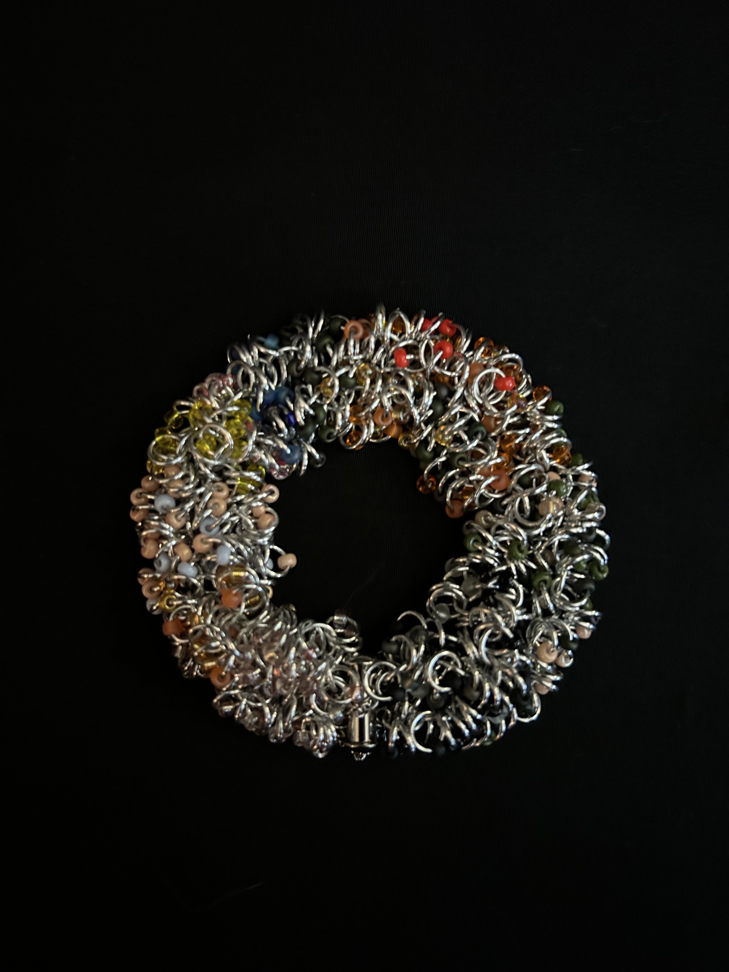 Blue Ridge Autumn bracelet laid flat on a dark background, showing the 20mm wide chainmaille pattern with red, gold, green, and orange Miyuki beads.