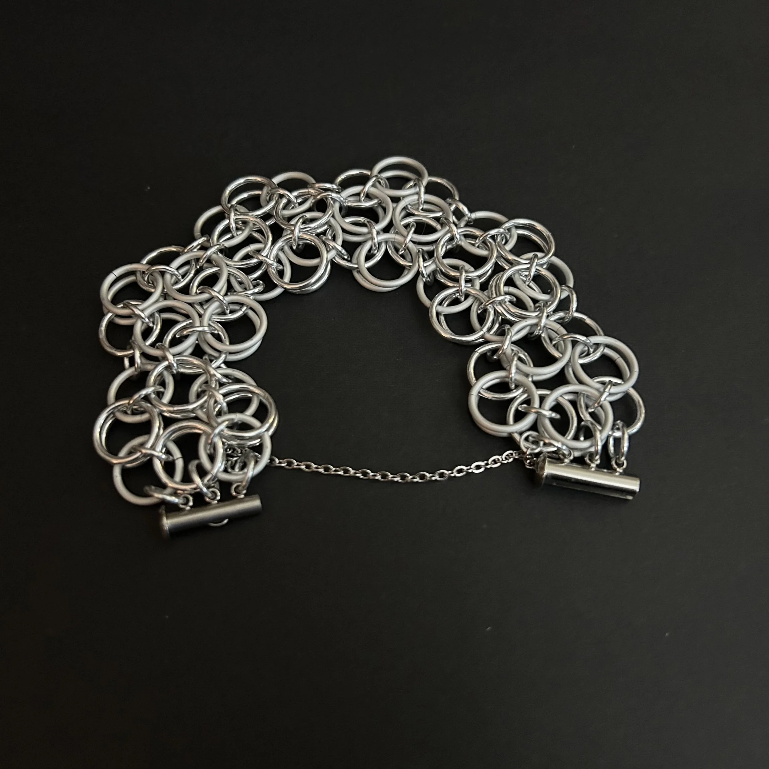 A chainmaille bracelet woven in a helm rosette pattern laid flat on a black background