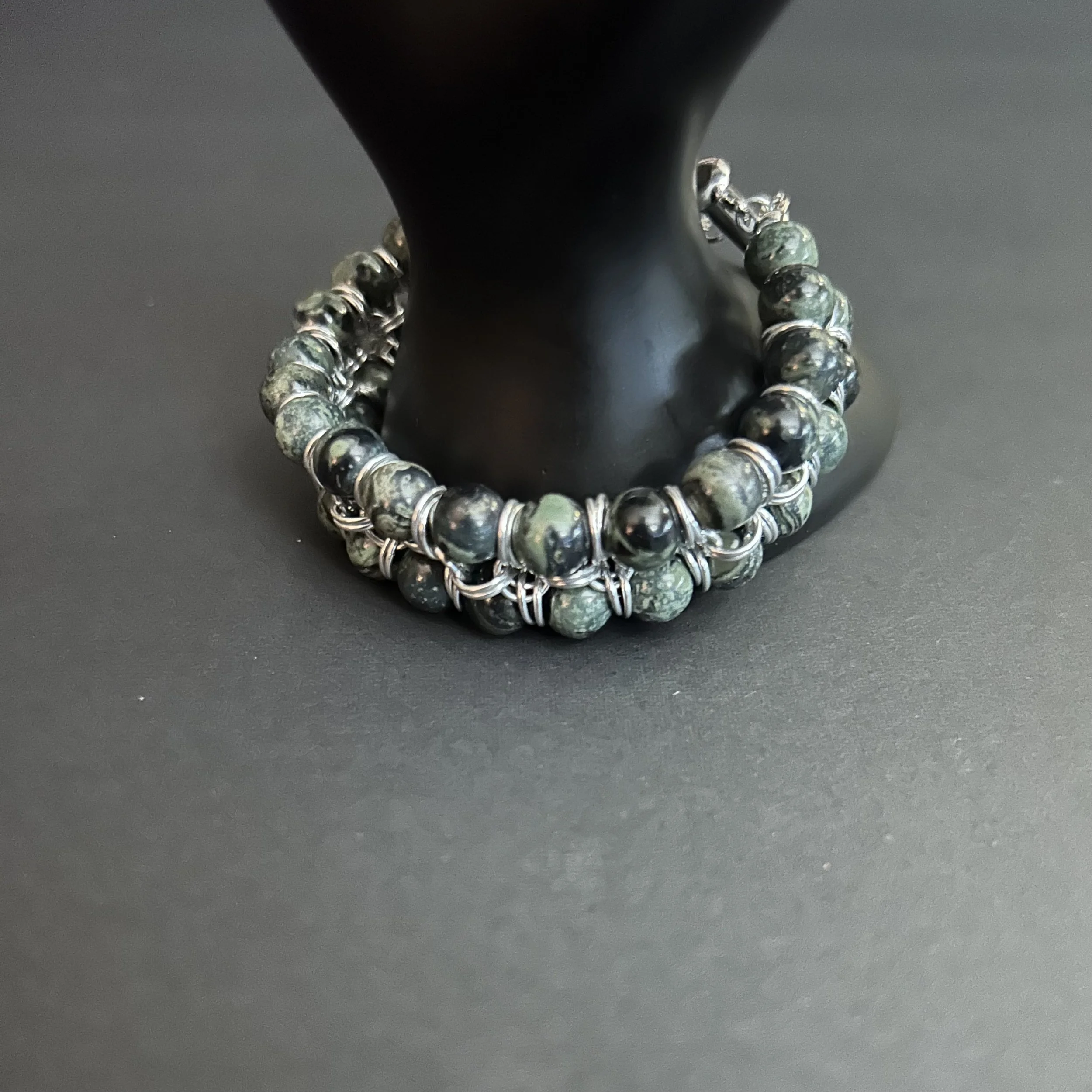 Double‑strand structure of the Kambaba Jasper and aluminum bracelet.on black hand prop