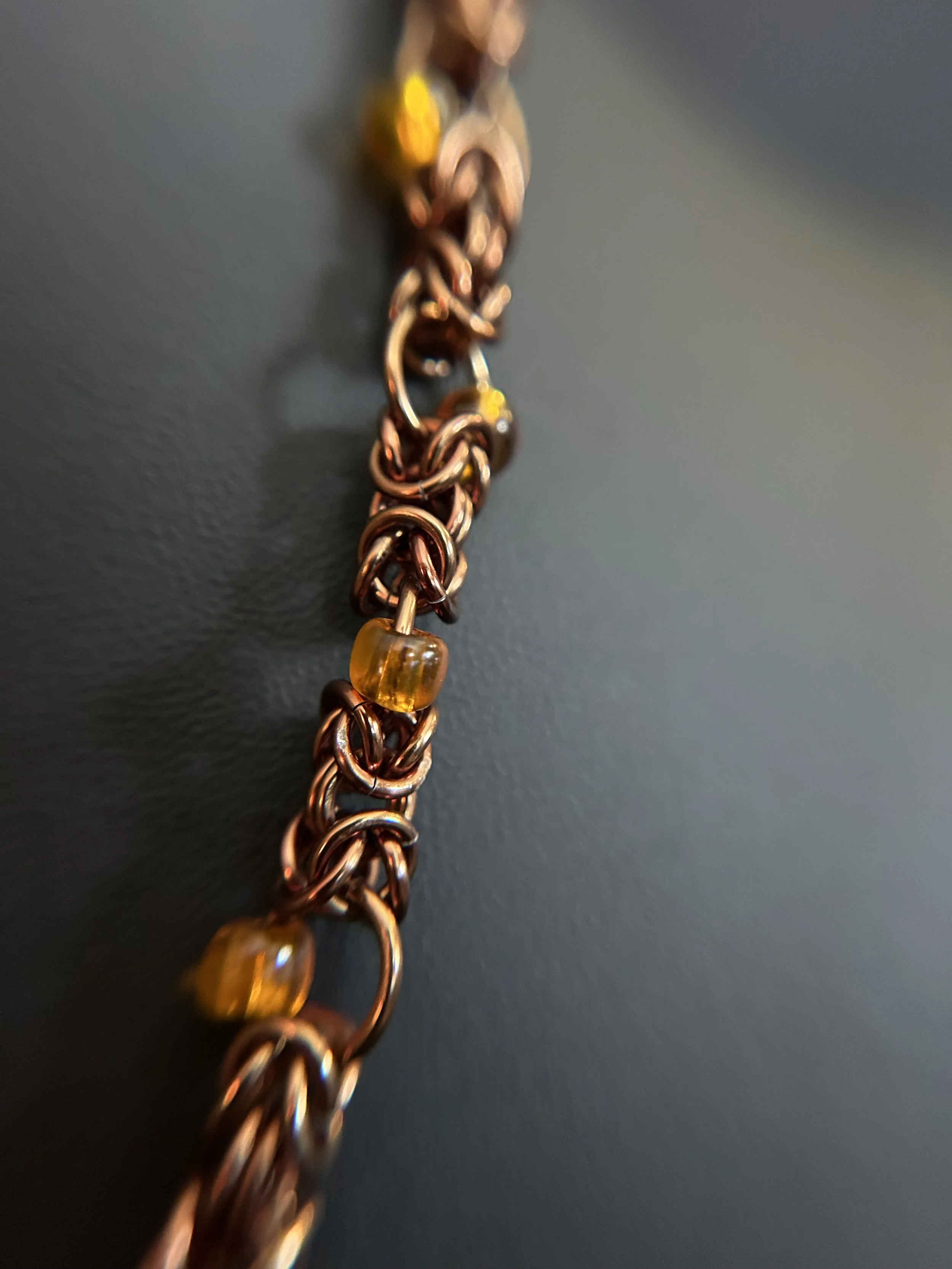 Close‑up of the necklace chain showing interwoven bronze‑colored links with small amber beads spaced along the weave.
