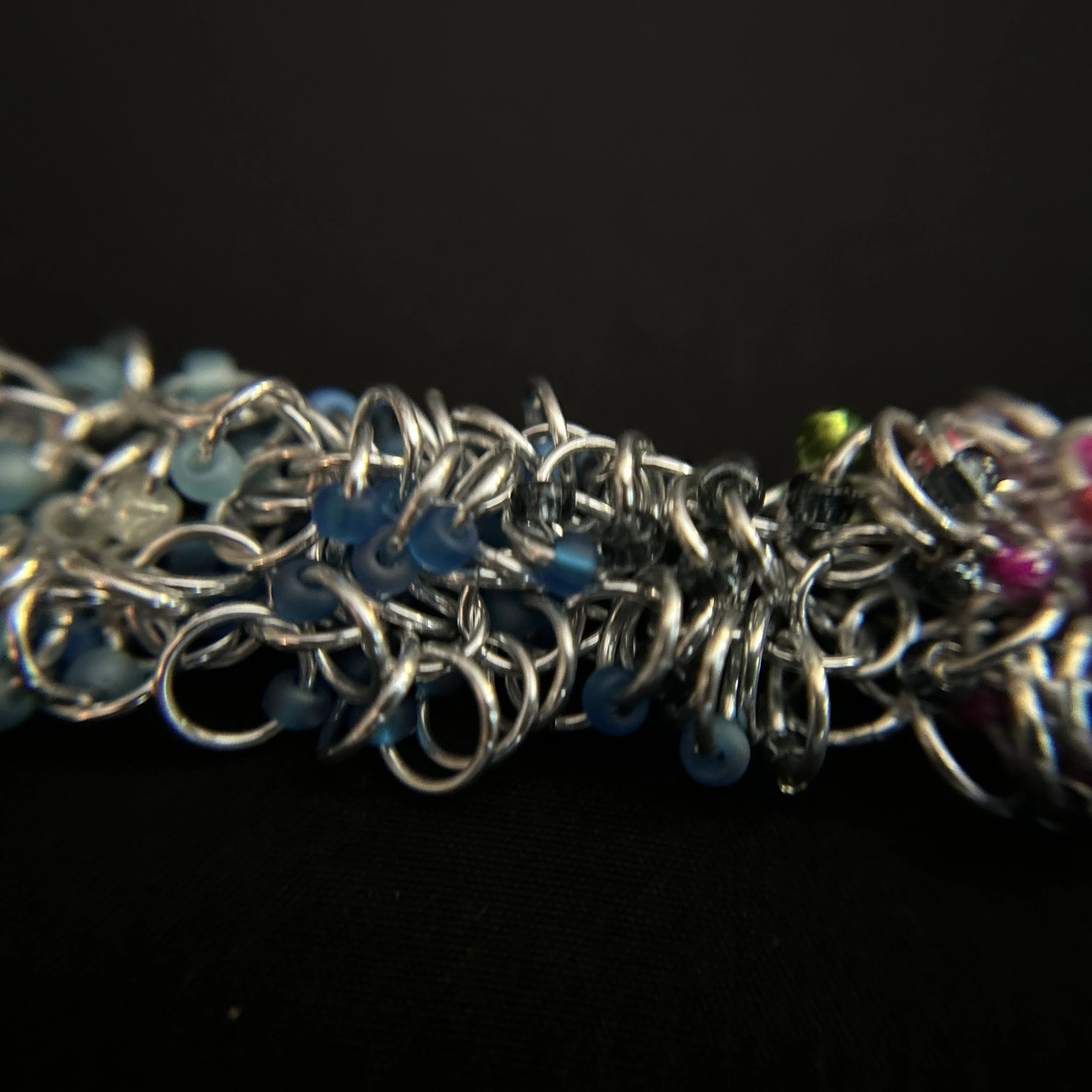 “Detail of the aluminum rings with blue, pink, green, yellow, and white beads.”