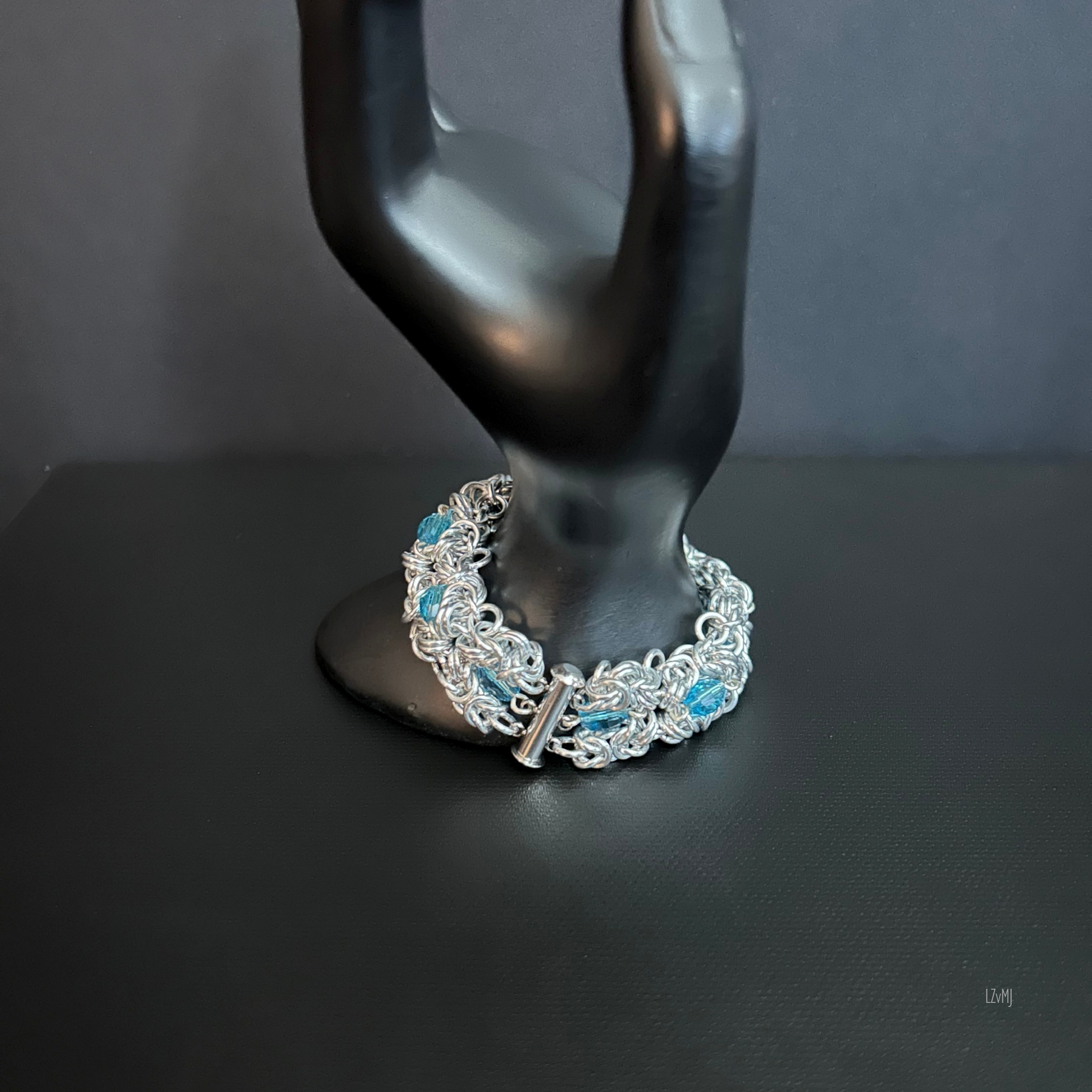 Turquoiseberry Byzantine bracelet on a black mannequin hand, featuring polished aluminum chainmaille and turquoise crystal accents with a cylindrical clasp