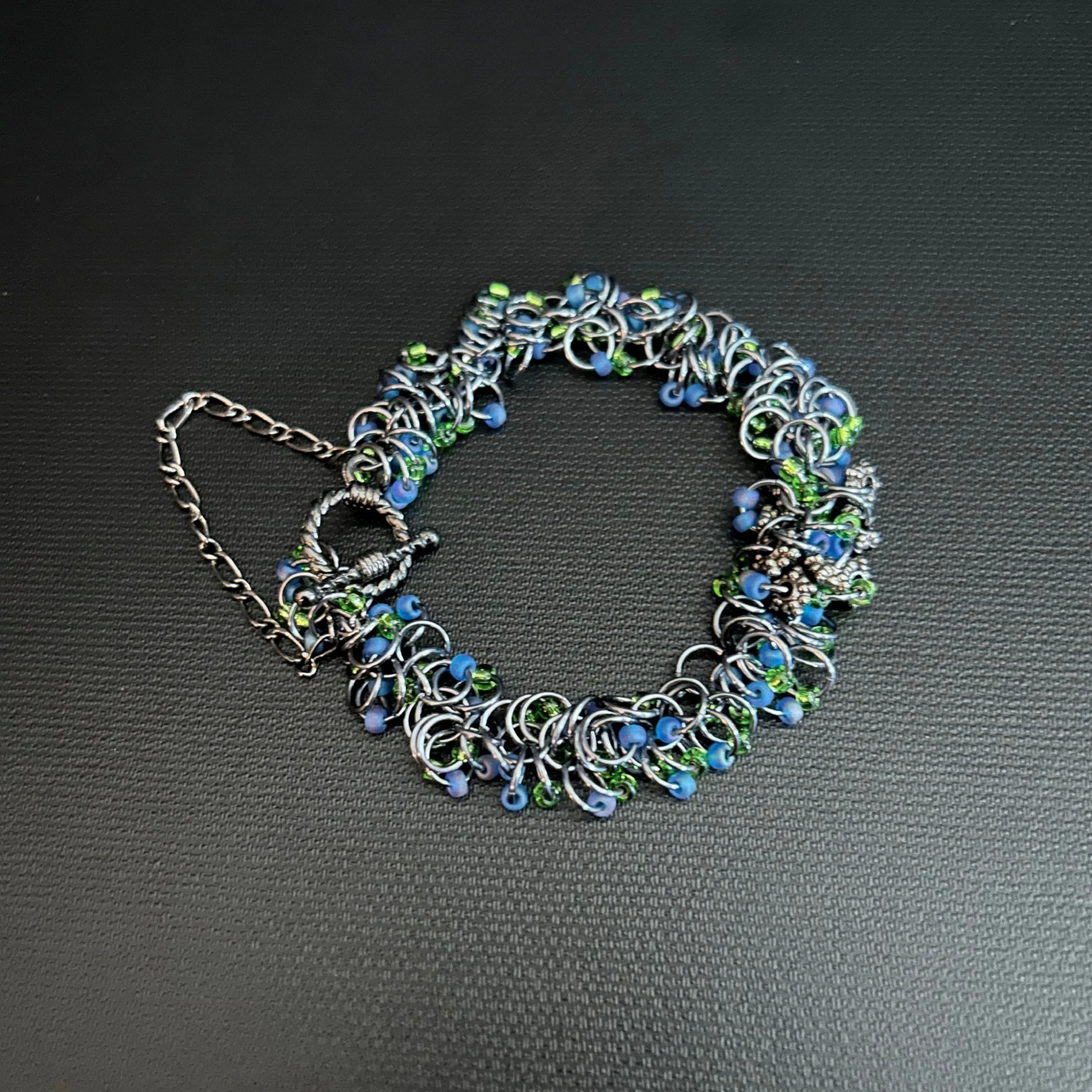 “Riverglint bracelet laid flat, showing Black Ice rings with blue and green Miyuki beads.”