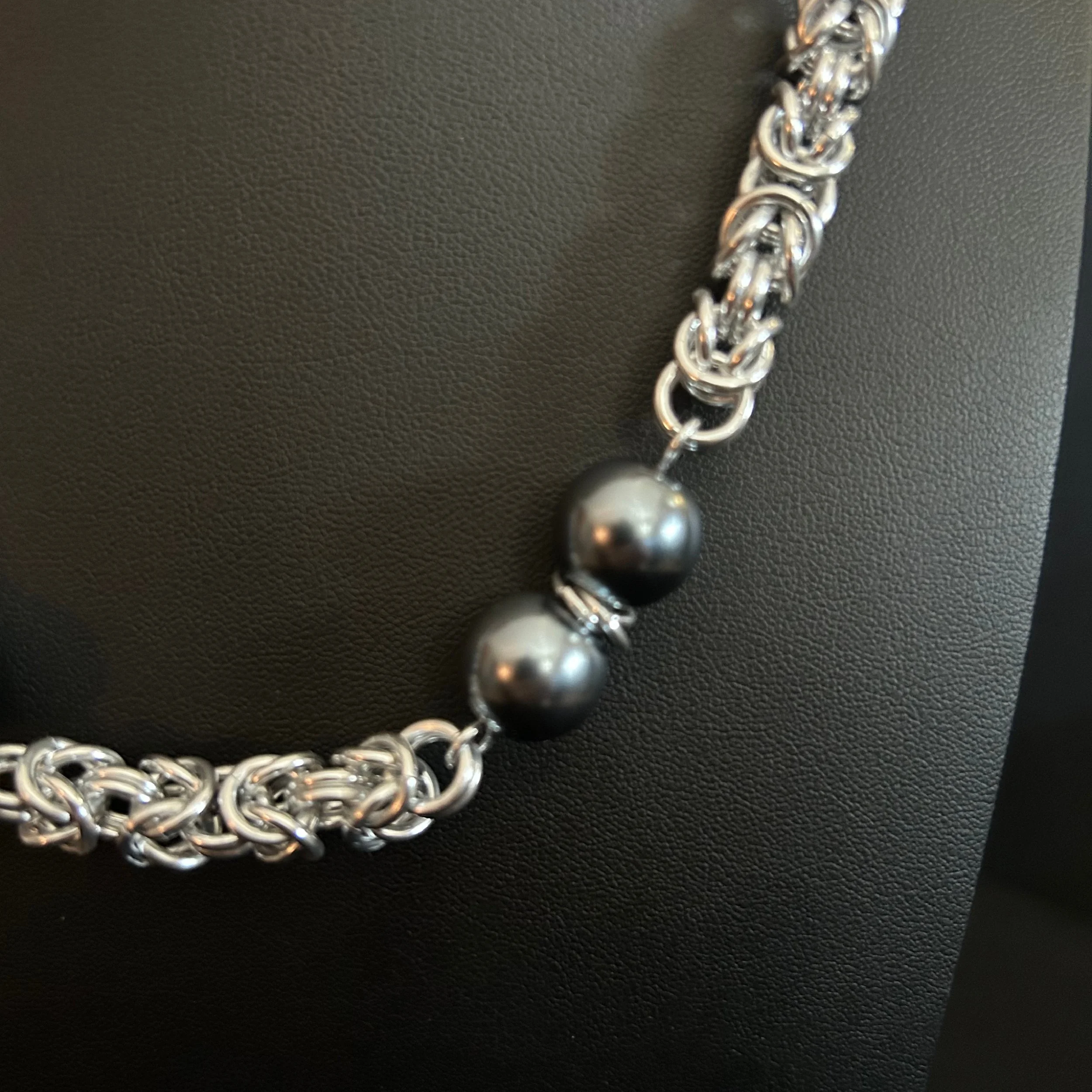“Detail of the aluminum rings and dark glass pearls in the chainmaille pattern.”