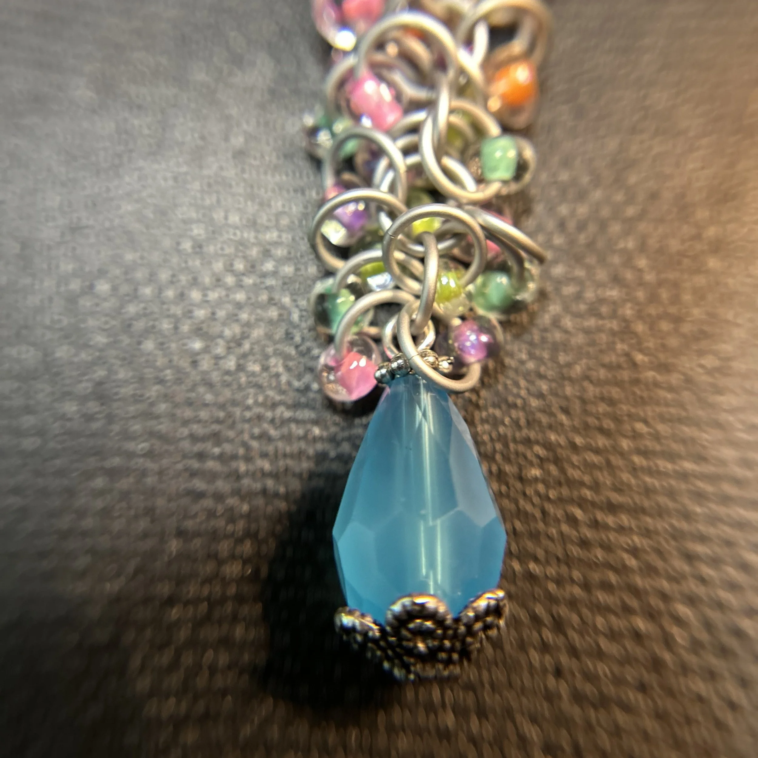 Closeup of pastel bead array and blue drop on a silver shaggy loop and Byzantine purse charm.