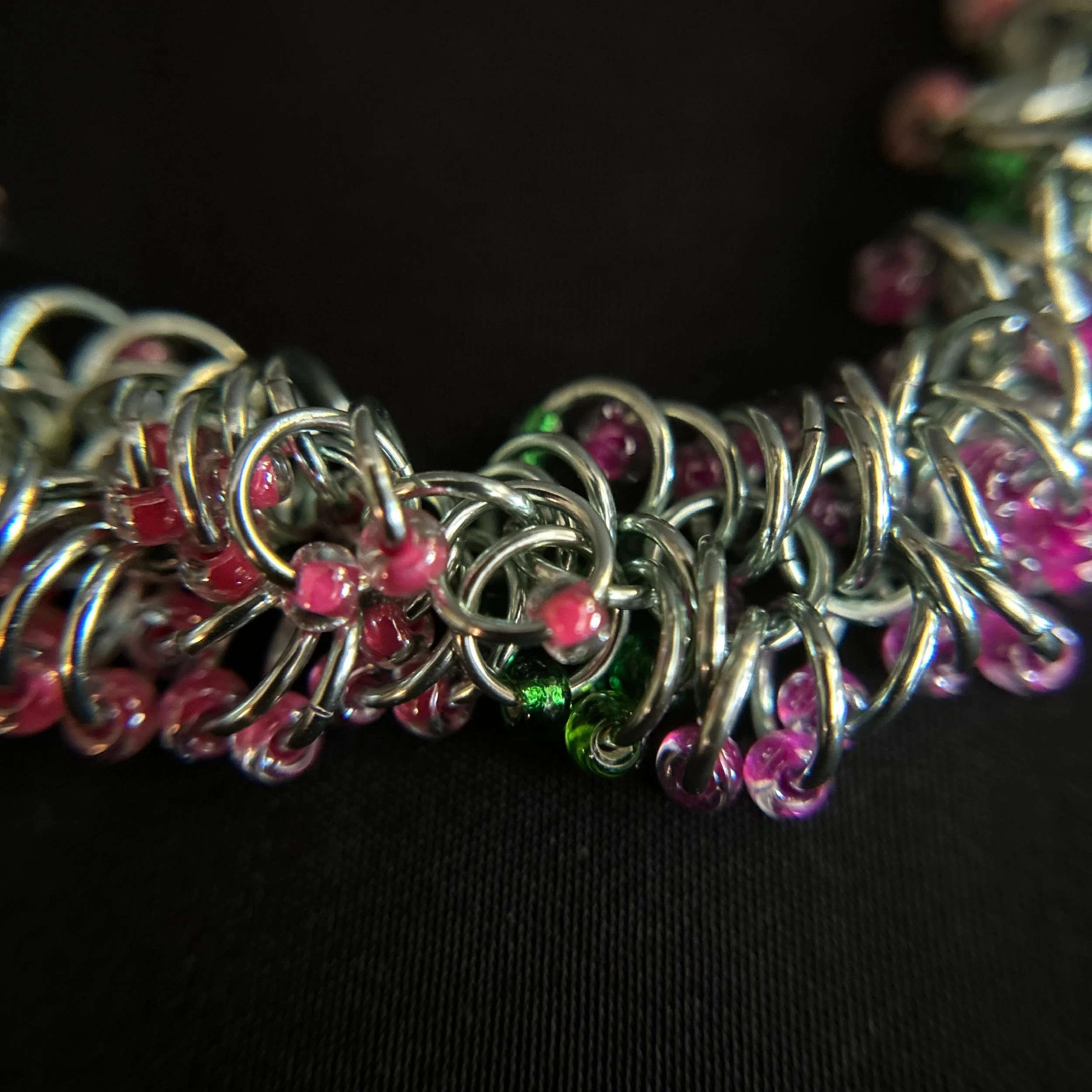 “Detail of the chainmaille rings with pink, green, and purple beads.”