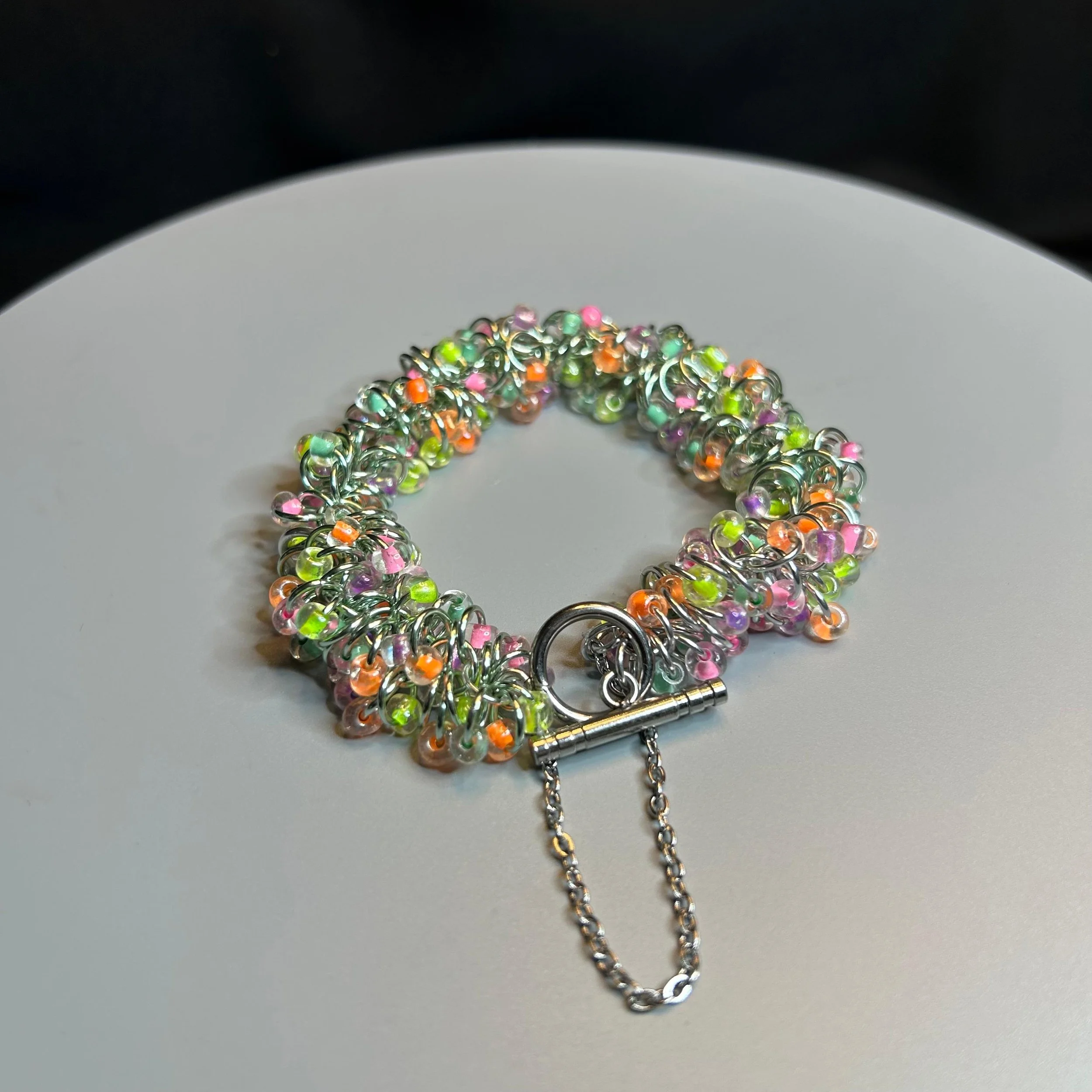 Bracelet laid flat with clasp closed, showing full chainmaille weave and pastel bead pattern.